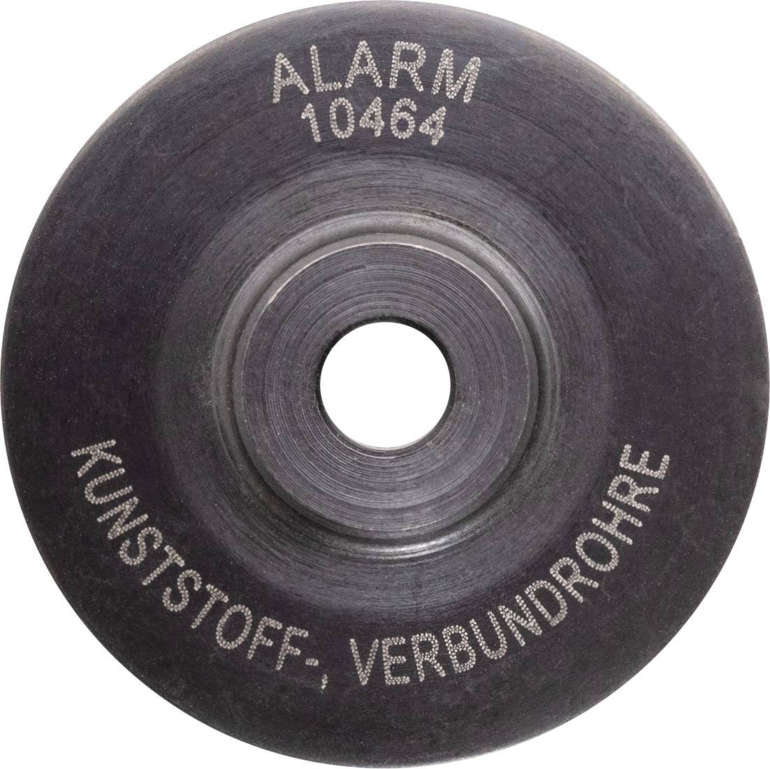 En sort cirkulær genstand med 'ALARM 10464 KUNSTSTOFF, VERBUNDROHRE' påskrevet, ser ud til at være en komponentdel, der muligvis er relateret til rørføringer eller alarmsystemer.