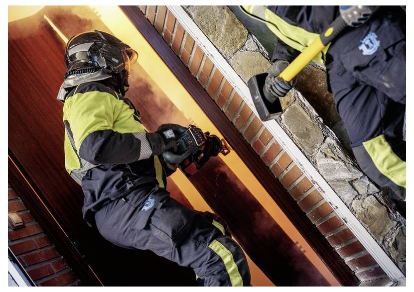 Brandmænd i beskyttelsesudstyr går ind i en røgfyldt bygning, hvor en holder en sav og en anden en økse, i en akut indsats.