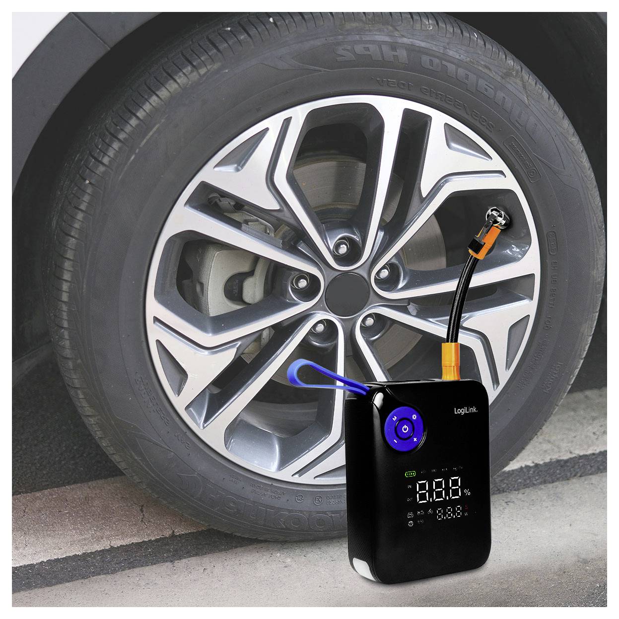 En bærbar dækpumpe ved siden af et bildæk, som viser digitale trykavlæsninger på sin skærm og fremhæver dens funktion og design.
