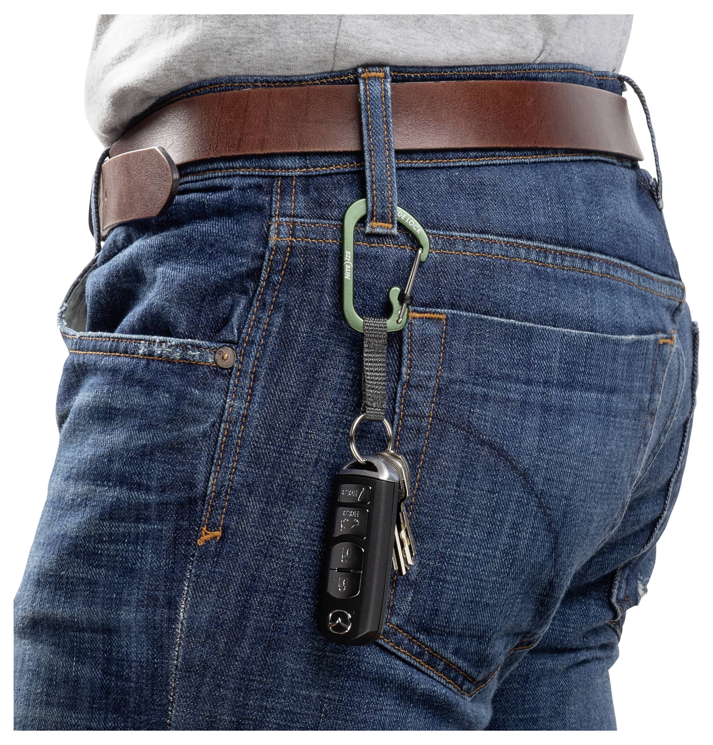 En person iført jeans og et brunt bælte har en nøglering fastgjort til bæltestroppen. Nøgleringen holder en bilnøglebrik og yderligere nøgler.