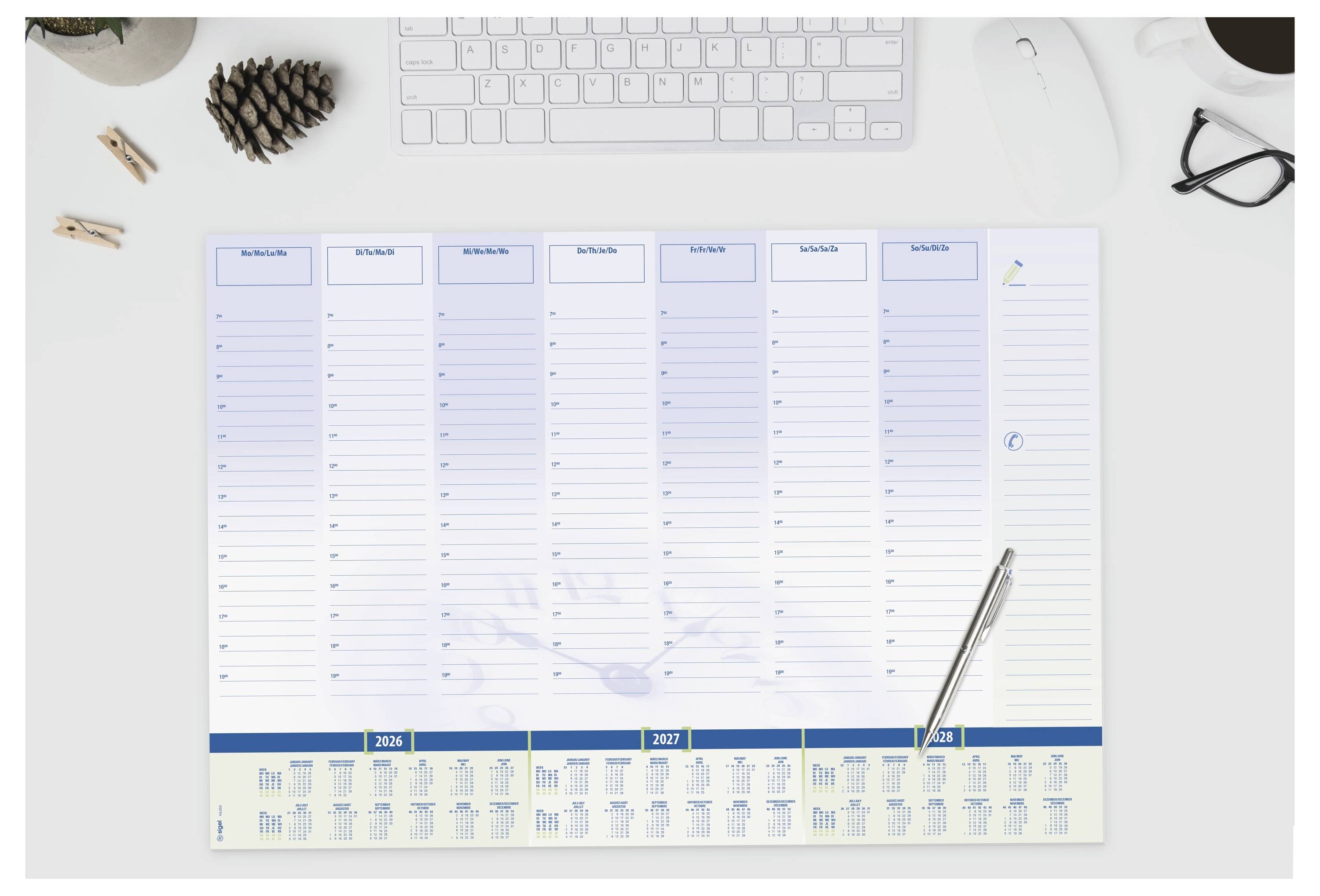 En skrivebordsk almanakplanlægger med kolonner mærket efter dage og en pen hvilende på den; et tastatur og en mus er i baggrunden.