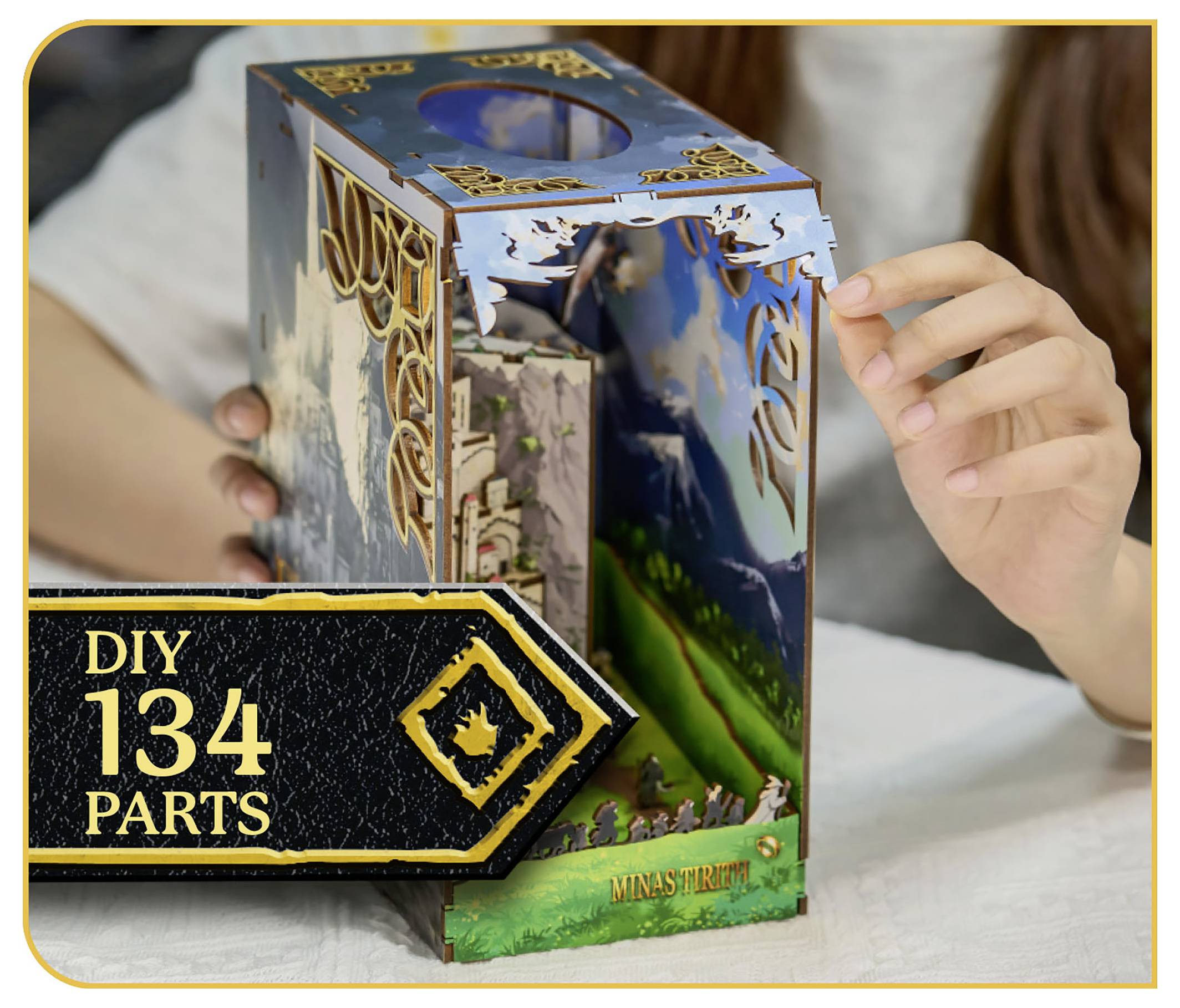 DIY 134-dele modelbyggesæt med en detaljeret Minas Tirith-scene, hvor en person samler strukturen, med en malerisk baggrund synlig.