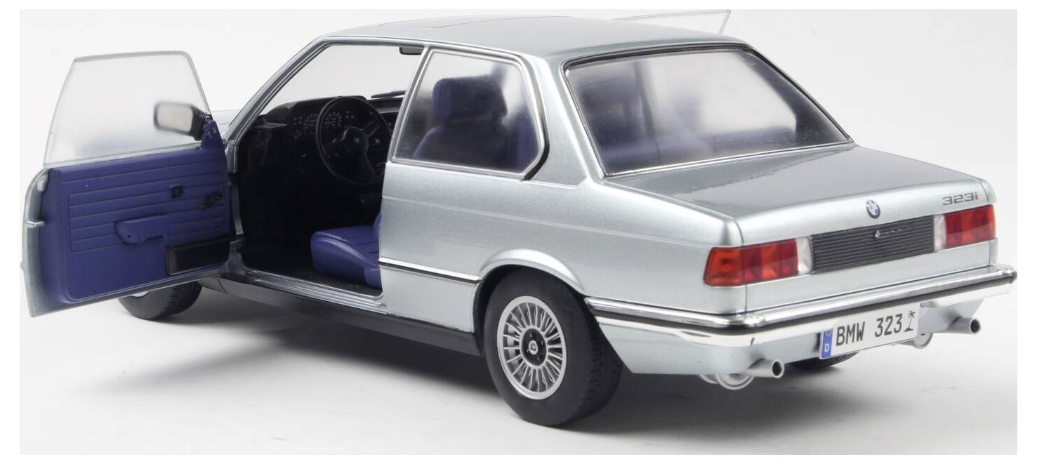 En sølvfarvet modelbil med åben førerdør, der viser et blåt interiør og nummerplade 'BMW 323i'.