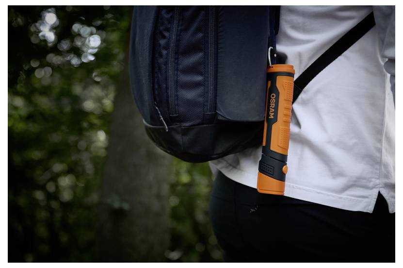 'En person med en sort rygsæk bærer en orange lommelygte, der er klistret fast til den, mens vedkommende går i en skov.'