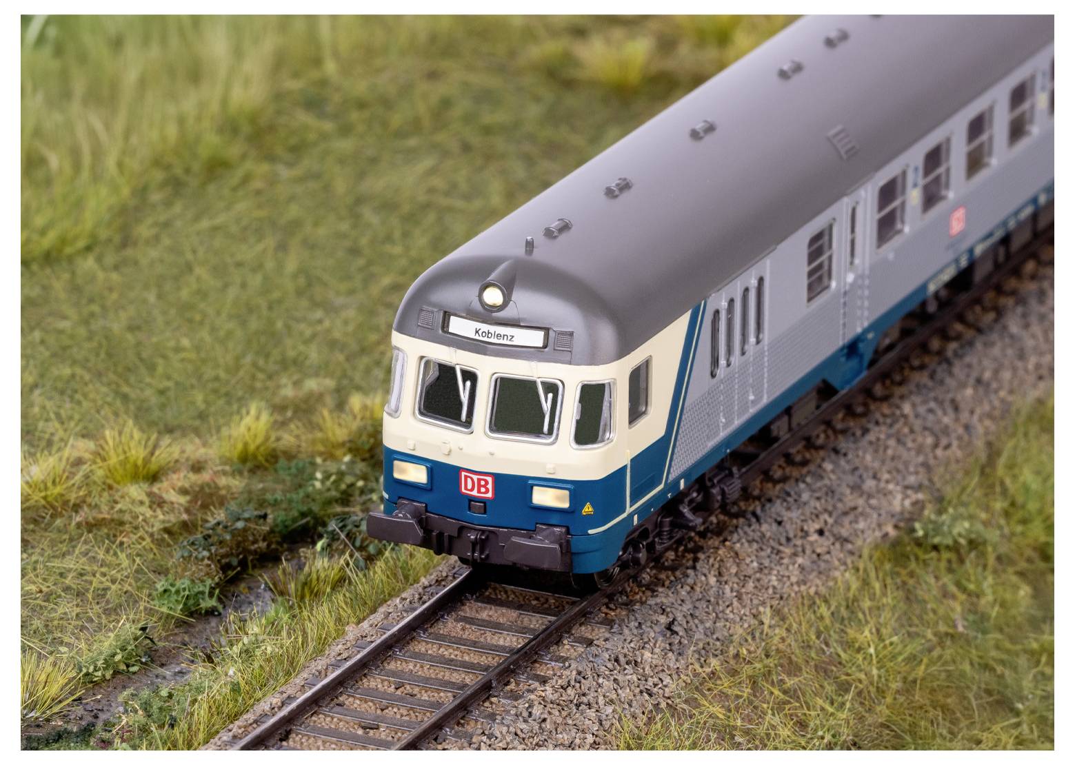 En model af en vintage passagertogvogn med en beige øvre halvdel og marmorødt nedre halvdel, detaljerede vinduer og indviklet undervogn.