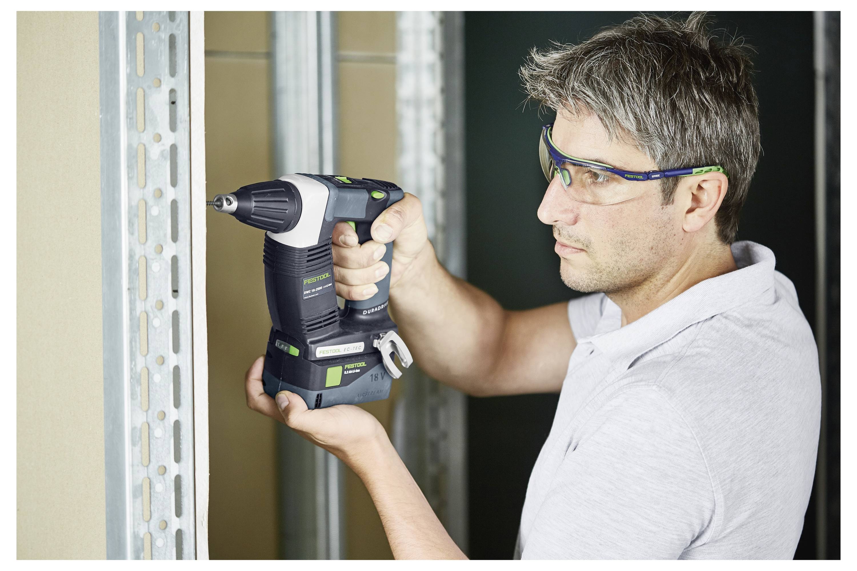 En person med sikkerhedsbriller bruger en elboremaskine på en metalramme på et byggeplads.