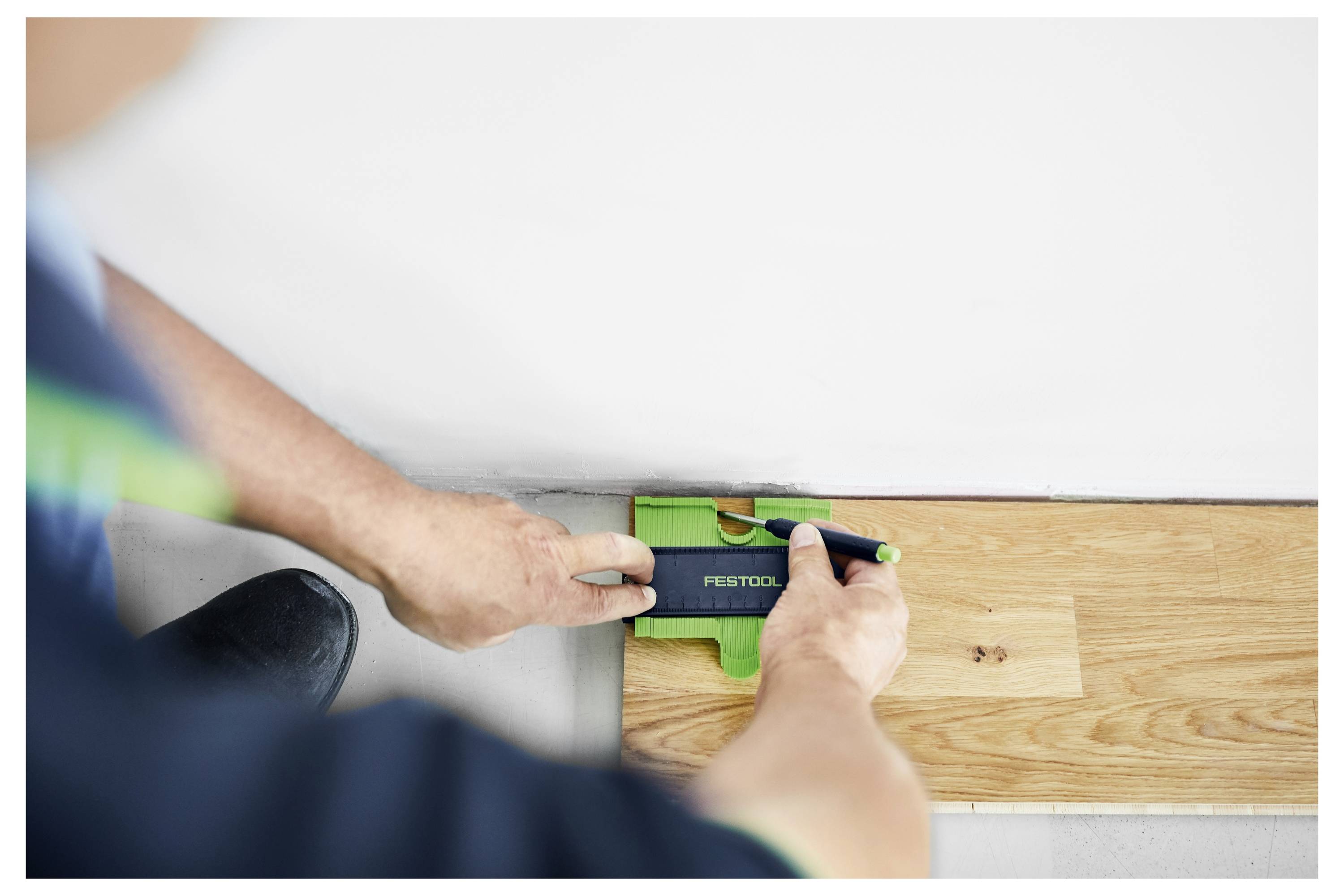 En person bruger en Festool elsesaksigsav til at skære i beton. Sågen er tæt på, hvilket understreger dens blad og den igangværende skæreproces.