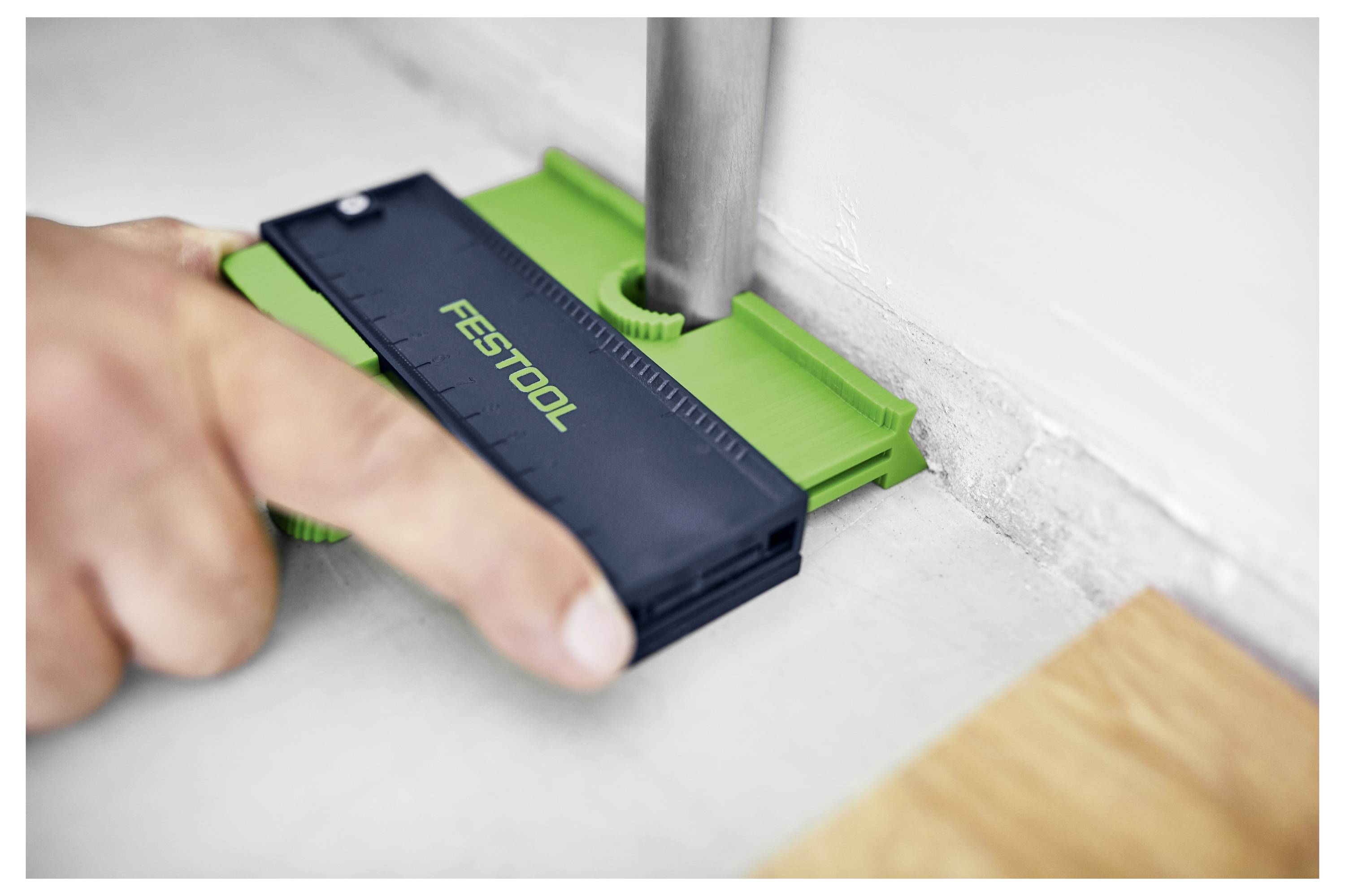 En hånd bruger en Festool konturmåler til at måle og gengive formen af et rør mod en væg nøjagtigt.