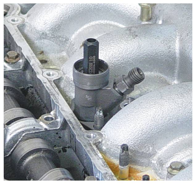 En motorkomponent med et synligt ventil og bolte, der virker metallisk og mekanisk, sandsynligvis en del af et forbrændingsmotorsystem.