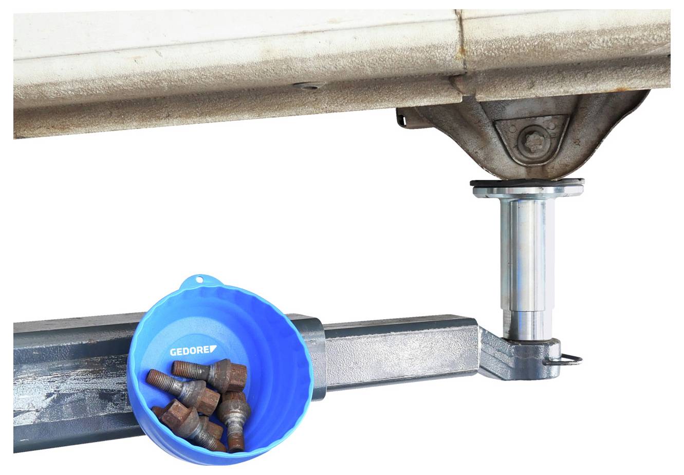 En blå beholder mærket 'GEDORE' indeholder flere bolte og hviler på en metalbjælke i et automobilløft. Undersiden af et køretøj er synlig.