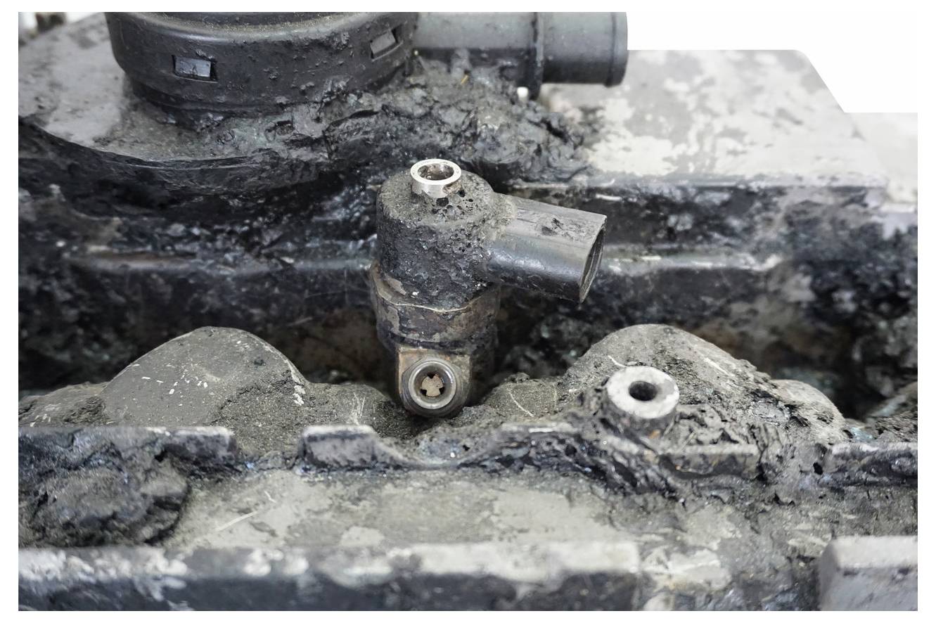 Et nærbillede af en kraftigt korroderet motorkomponent med synlig rust og smuds, som fremhæver forringelse og skade på dens overflade.