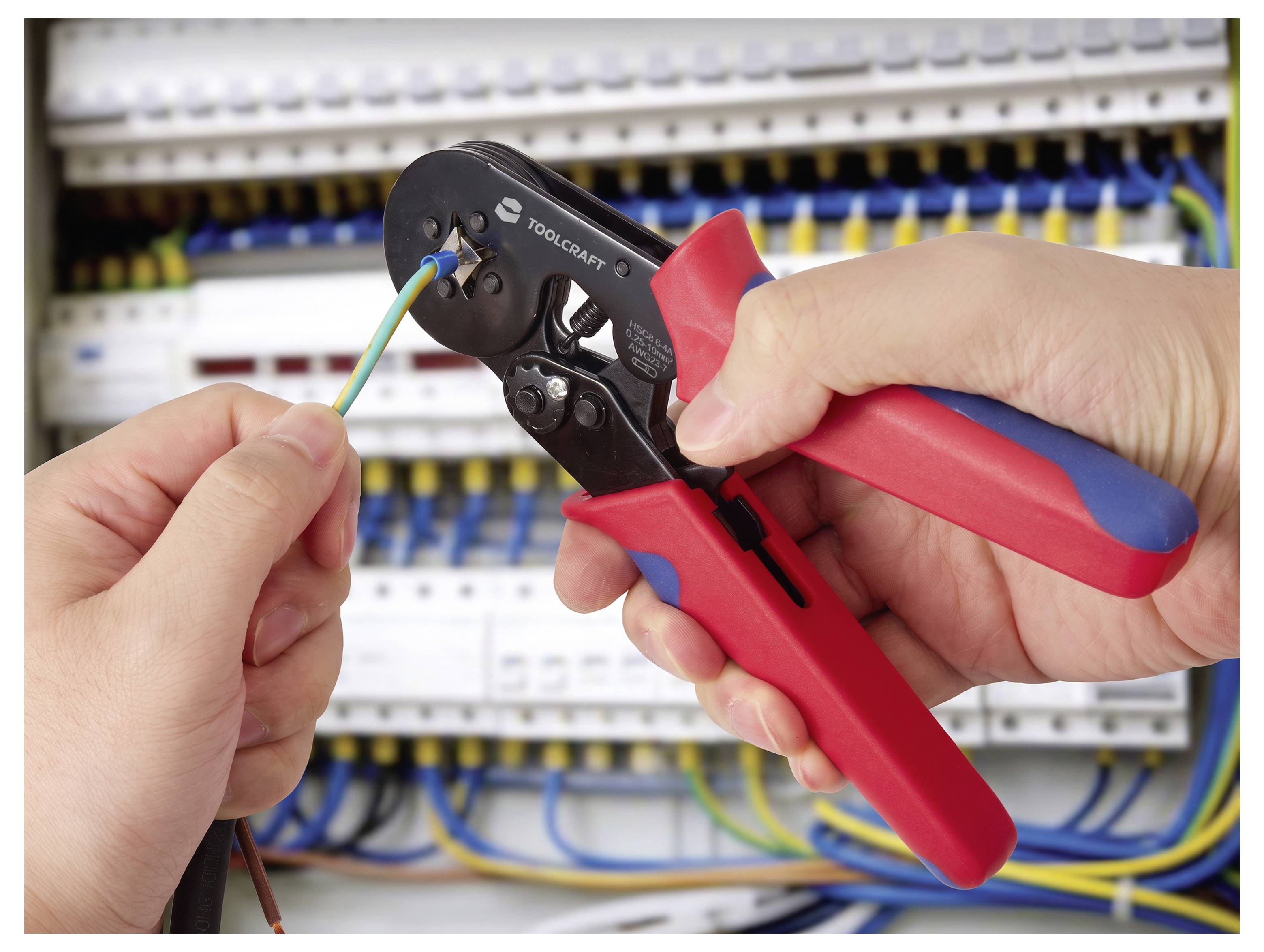 Hænder bruger trådstribber-tang til at strippe en ledning i et elektrisk panel med forbundne klemrækker.
