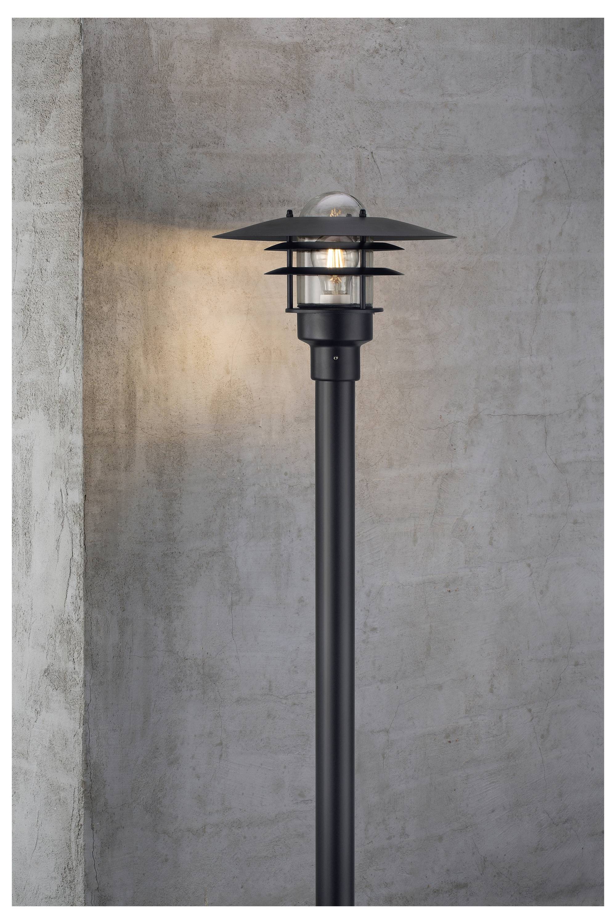 En moderne udendørlampe monteret på en betonmur, der udsender varmt lys. Lampen har et elegant, minimalistisk design med cirkulære metalskærme.