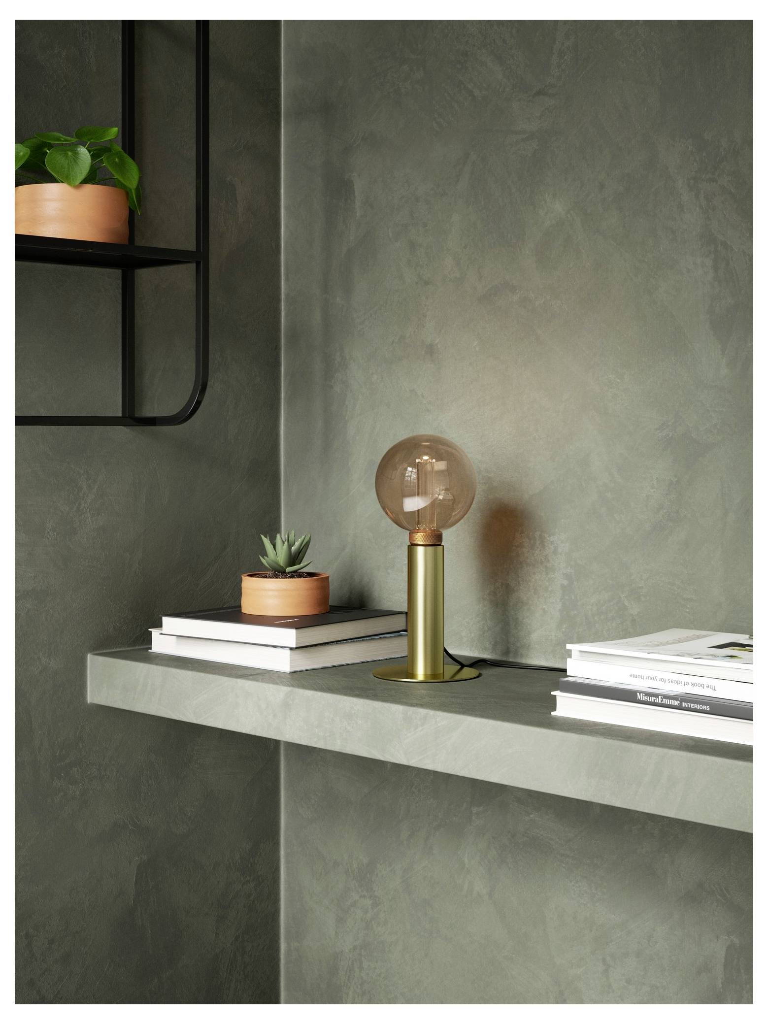 En minimalistisk hylder med en globuslampe, bøger og små potteplanter mod en struktureret grå væg.