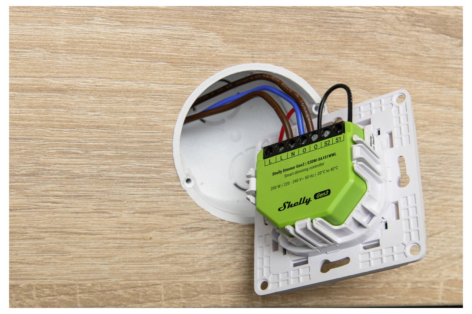 En elektrisk kontakt med eksponeret ledning monteret på en træoverflade. Kontakten er mærket "Shelly Pro" og ser ud til at være under installation.