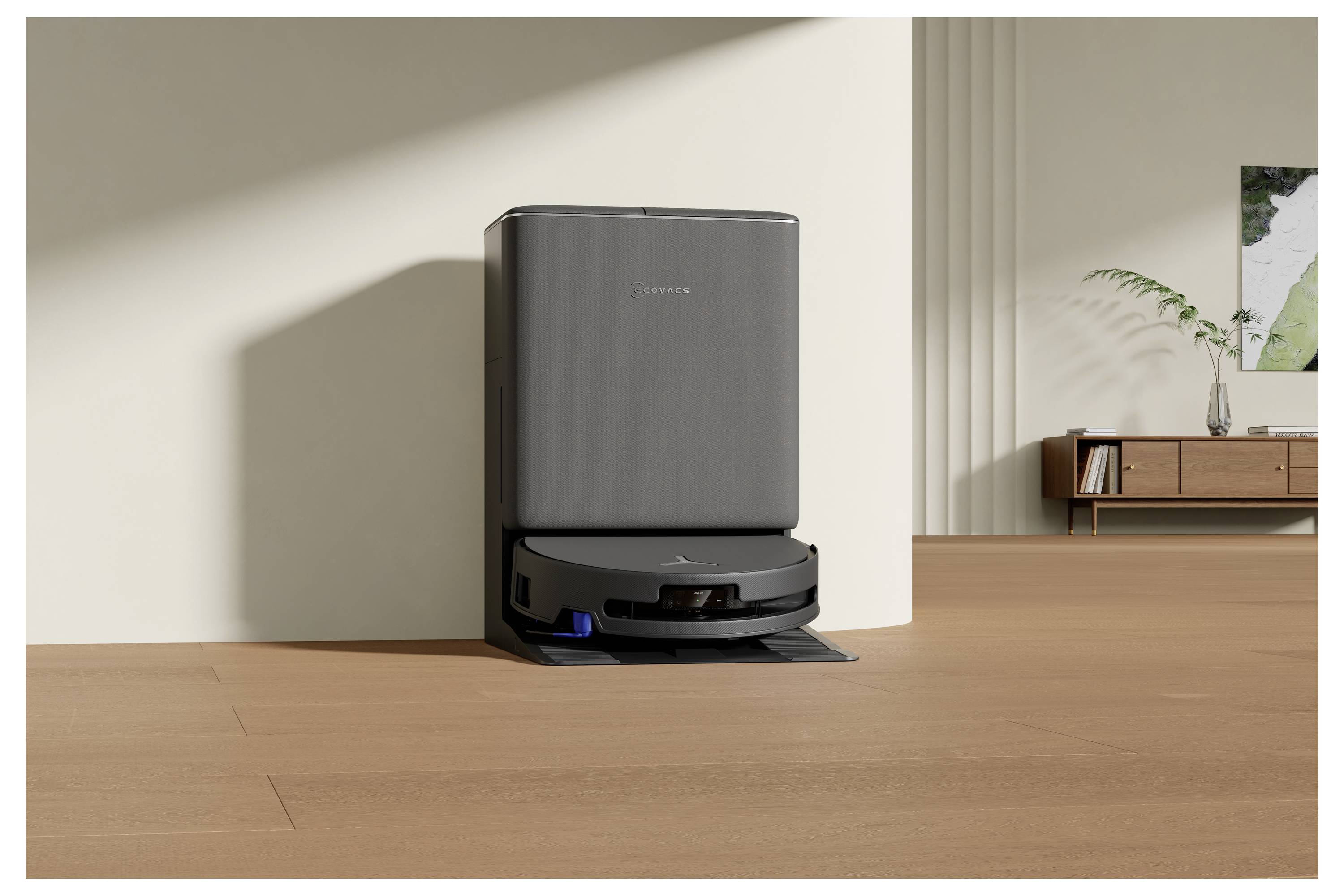 'Robotstøvsuger i et moderne stue, dockt i en opladningsstation mod en beige væg, træbund og minimalistisk møbler.'
