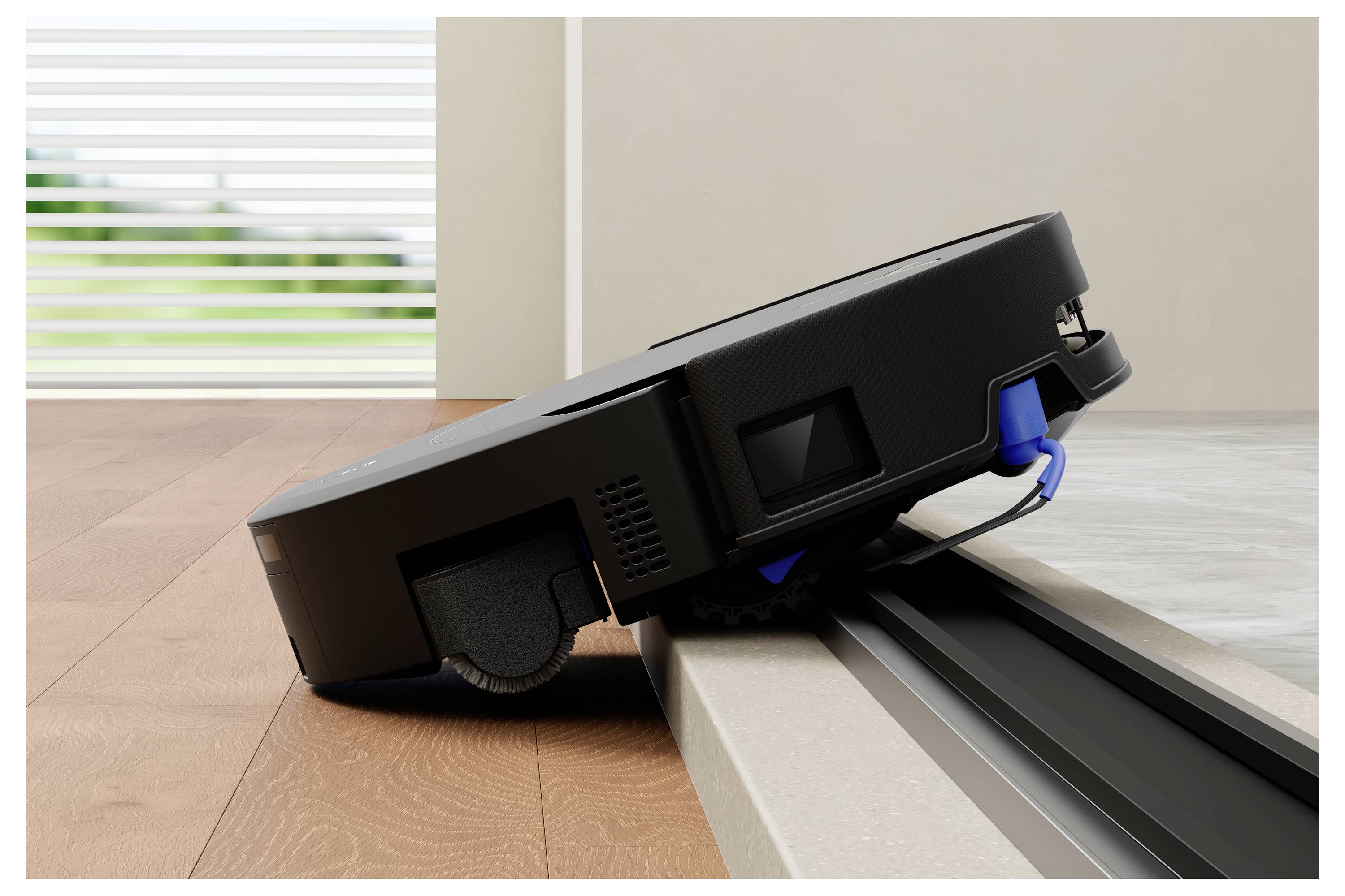 En sort robotisk støvsuger navigerer over en lille tærskel fra et træ gulv til en flisebelagt overflade i et lyst rum.