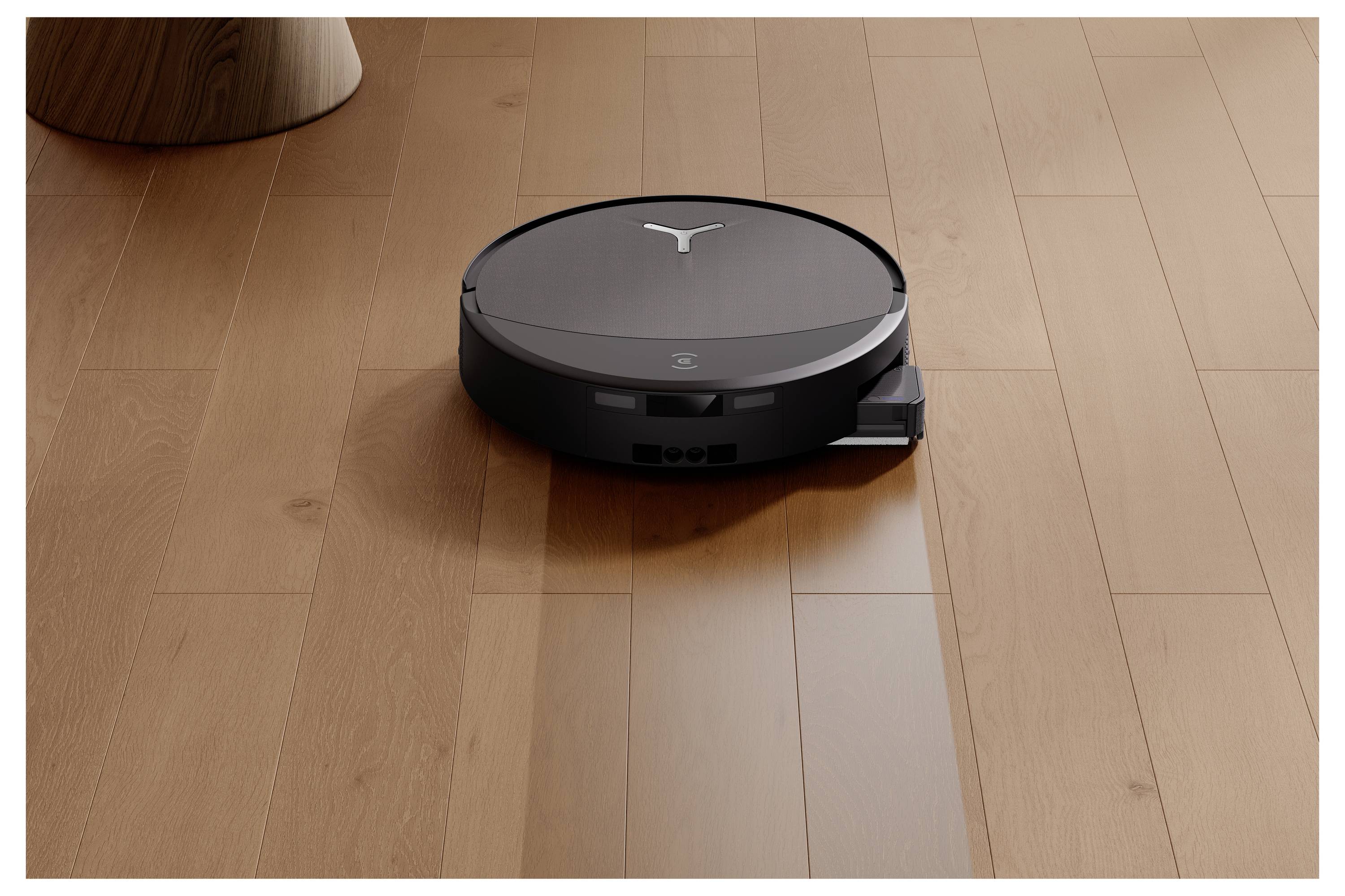 En rund robotkstøvsuger på træ gulv, der navigerer autonomt nær et møbelbens ben.