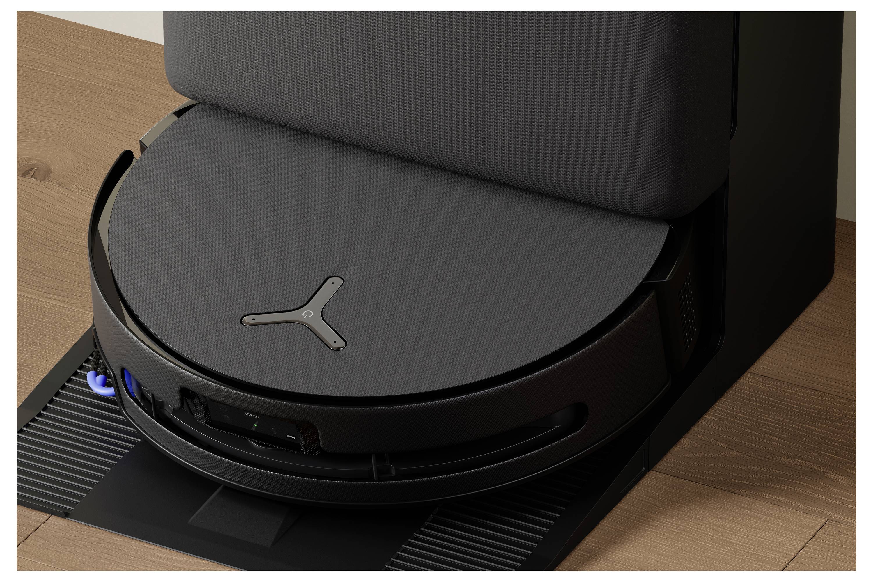 'En robotstøvsuger tilsluttet ved sin ladestation på et trægulv.'