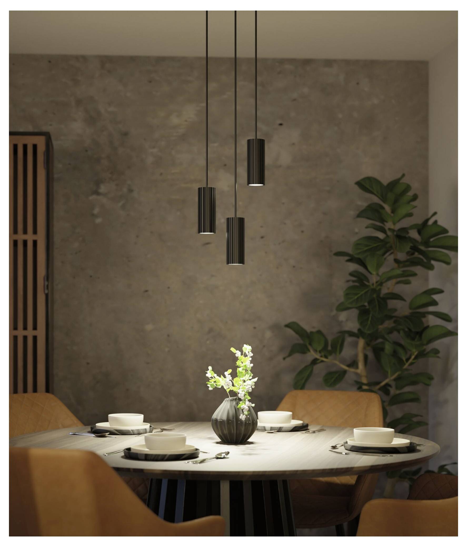 Moderne spisestue med et rundt bord dækket til fire personer, hængende pendullamper, en vase som centerpiece og en højt pottet plante.