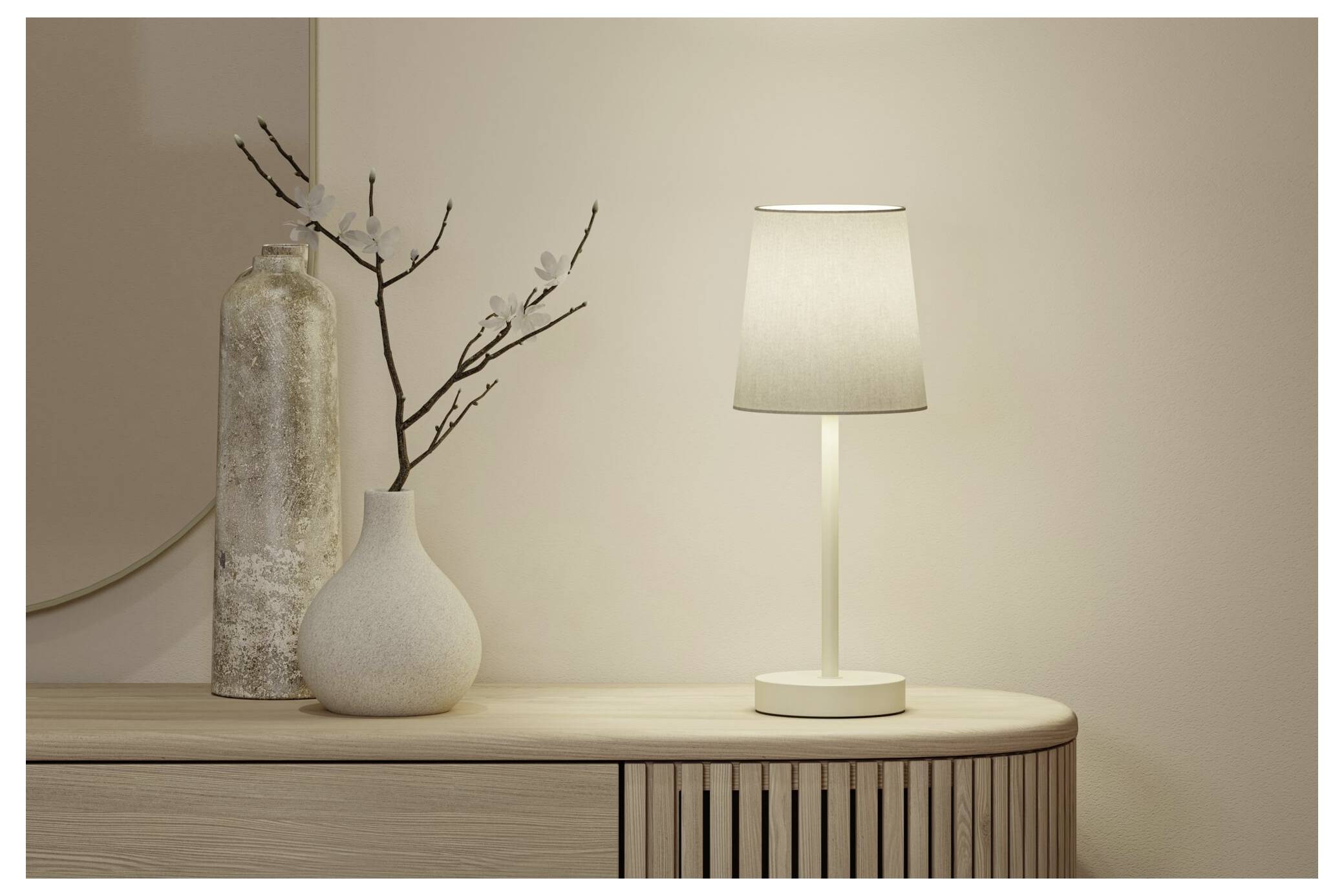 En tændt moderne bordlampe står på et træskab ved siden af dekorative vaser og grene mod en plain beige væg.