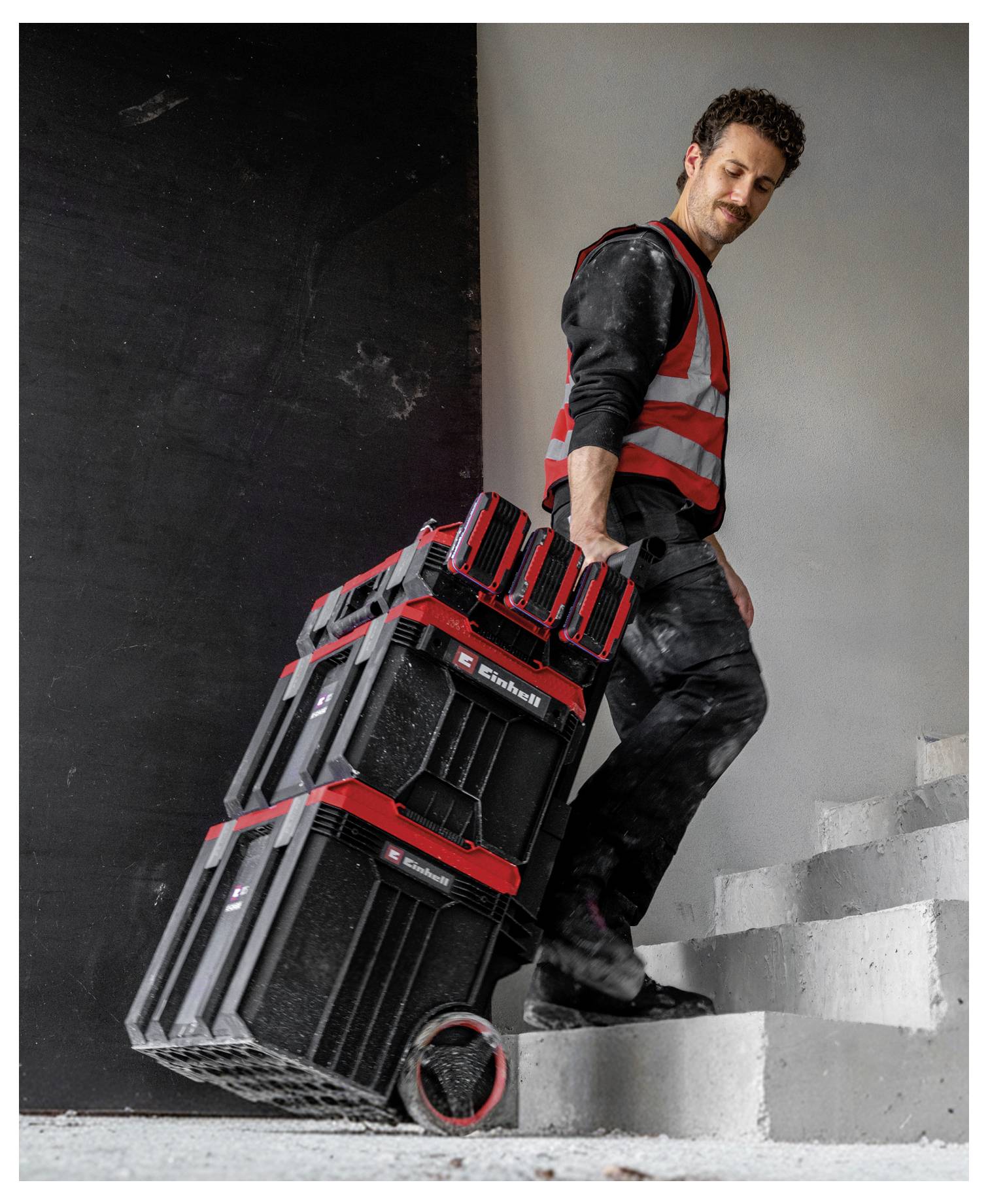 Arbejder på byggeplads bærende stablet værktøjskasser op ad ufærdige trapper