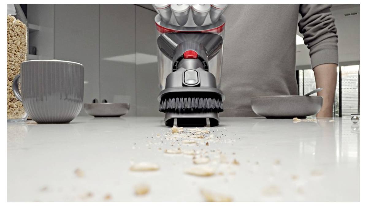 Håret vakuum renser cerealrester fra en bord ved siden af skåle og en kop på et køkken.