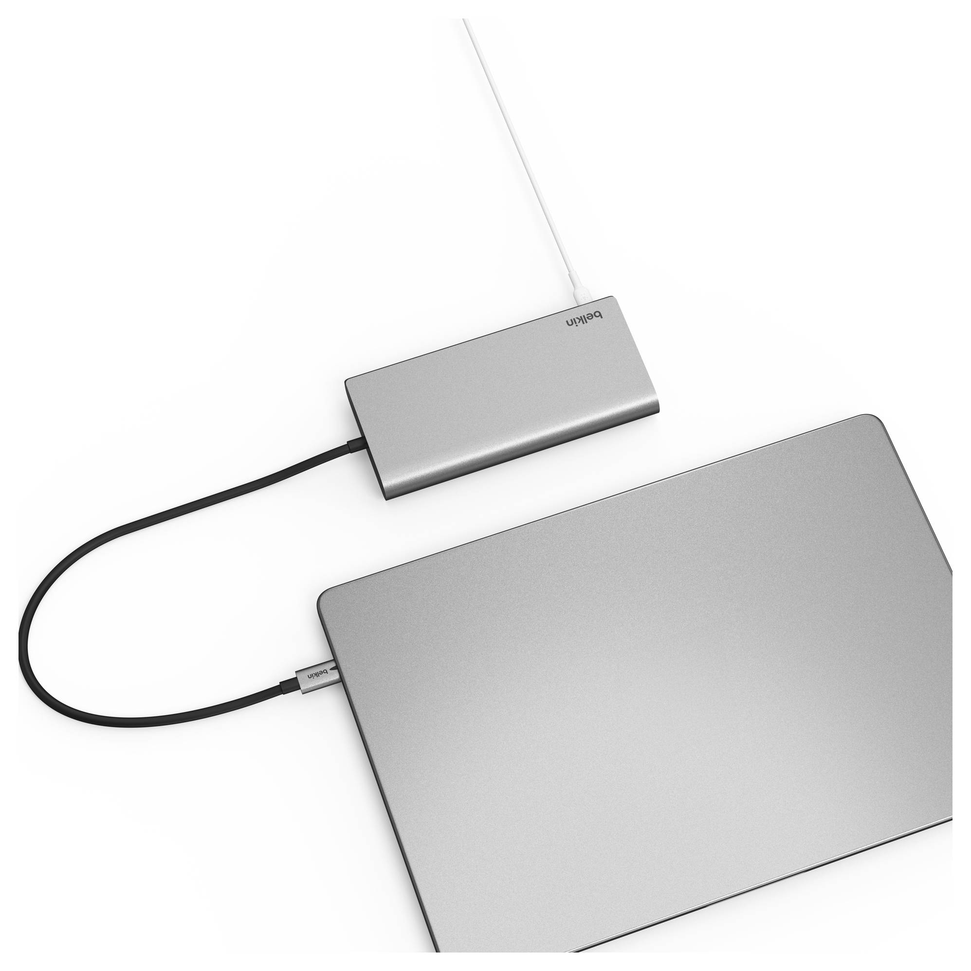 Sølvfarvet bærbar computer forbundet med sort kabel til en lille sølvfarvet adapter eller hub med hvidt kabel tilsluttet, vist på hvid baggrund.