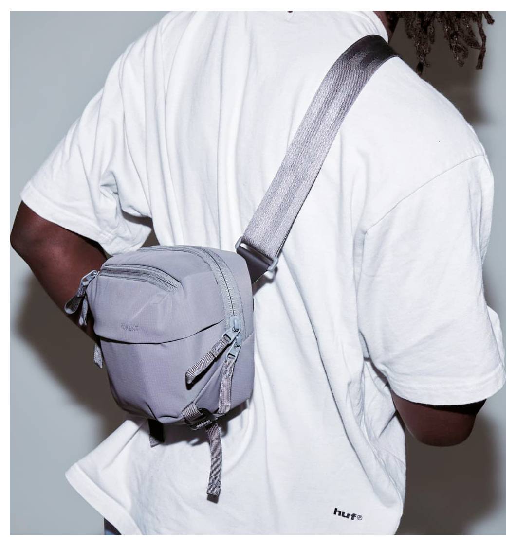 Person iført en hvid T-shirt med en grå crossbody slyngtaske på ryggen.
