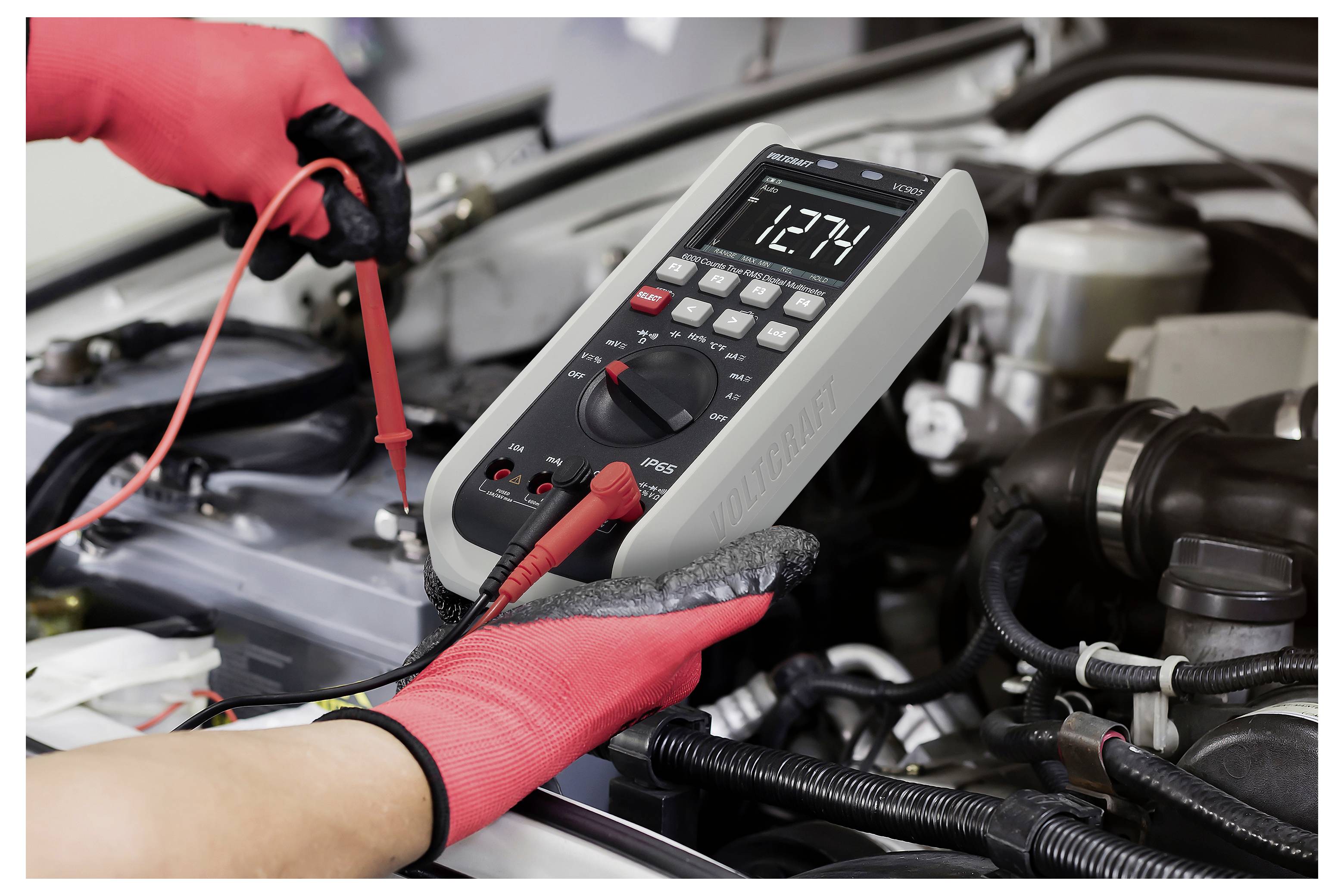 Mekaniker bruger et digitalt multimeter til at teste et bilbatteri i en motorrum.