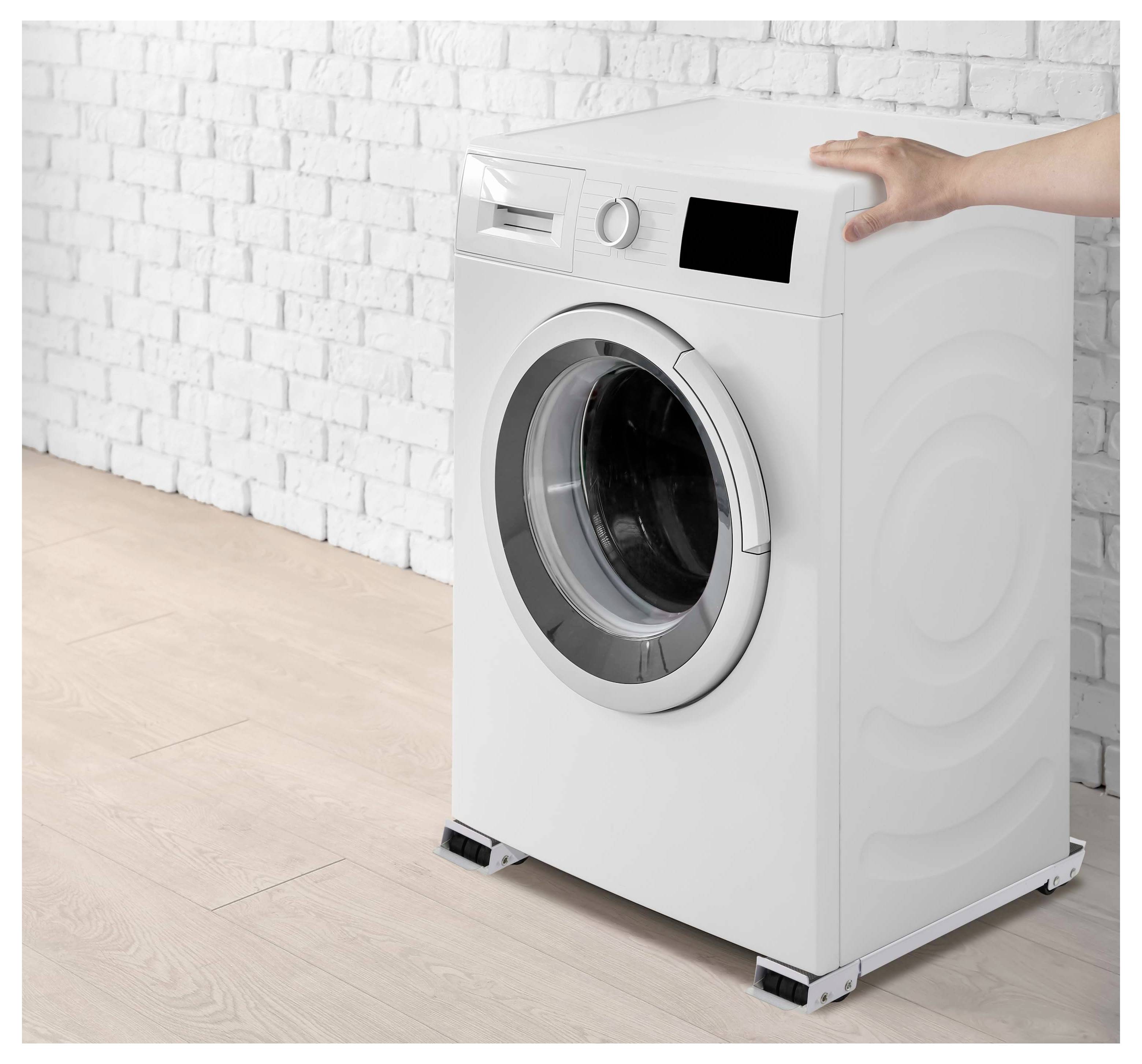 En hånd holder en hvid frontlæsser-vaskemaskine steady mod en hvid mursten væg i et lyst rum.