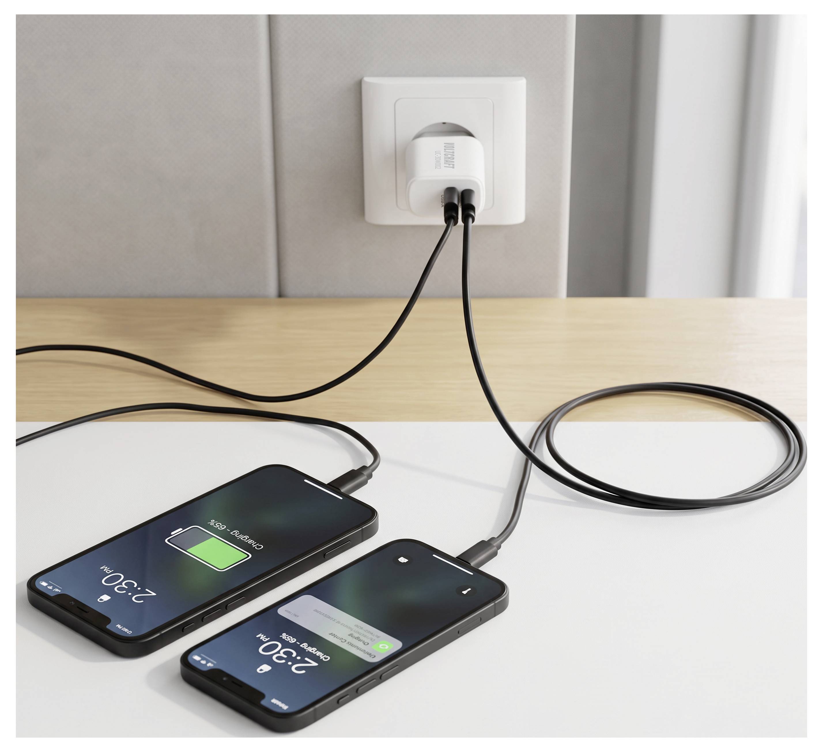 To smartphones, der oplades på et bord fra en stikkontakt, med batterisymboler, der indikerer aktiv opladning.