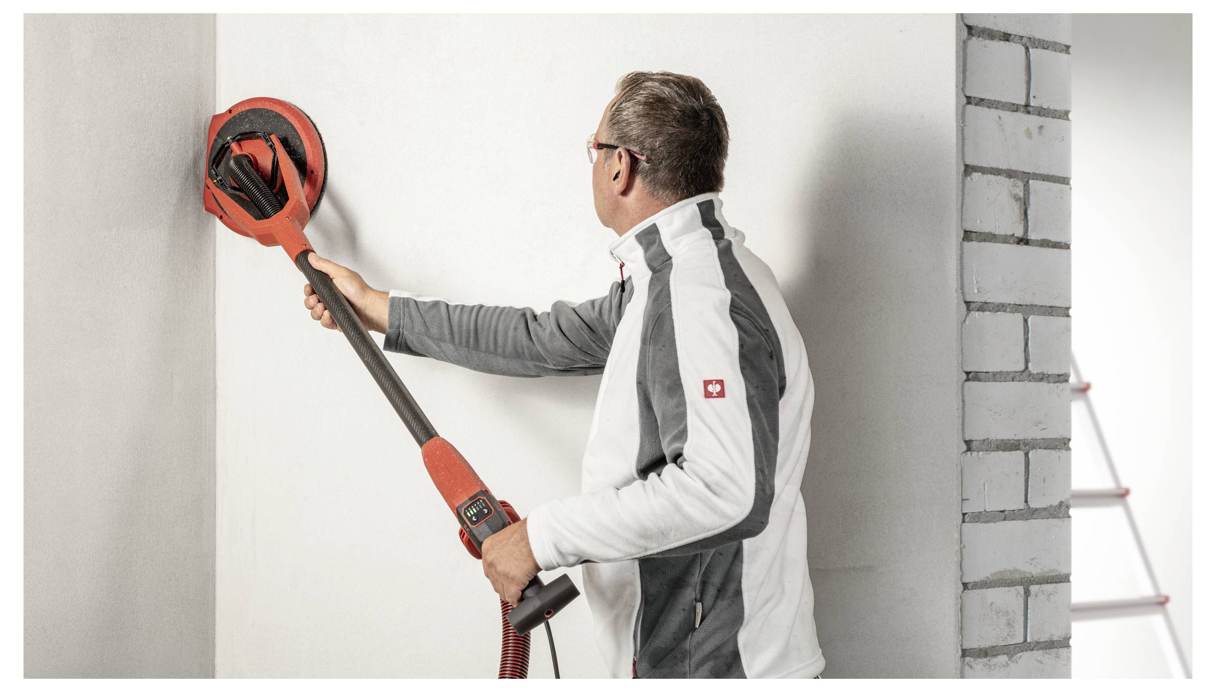 En mand sliber en væg med en håndholdt elektrisk gipspladesl­iber under indvendig renovering.
