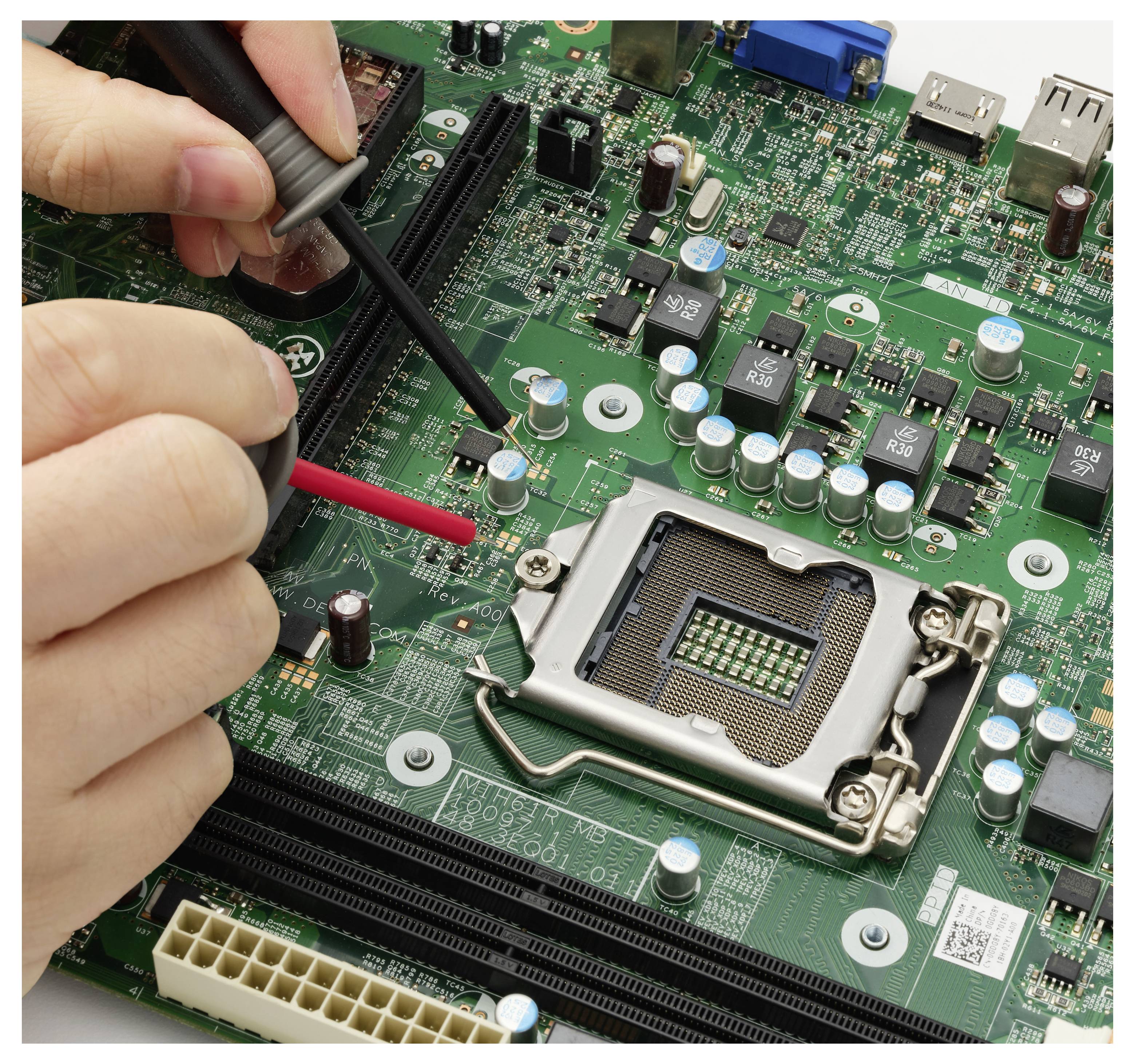 Hænder bruger testsondes på et computermoderboard nær CPU-soklen, kontrollerer elektroniske komponenter på kredsløbskortet.