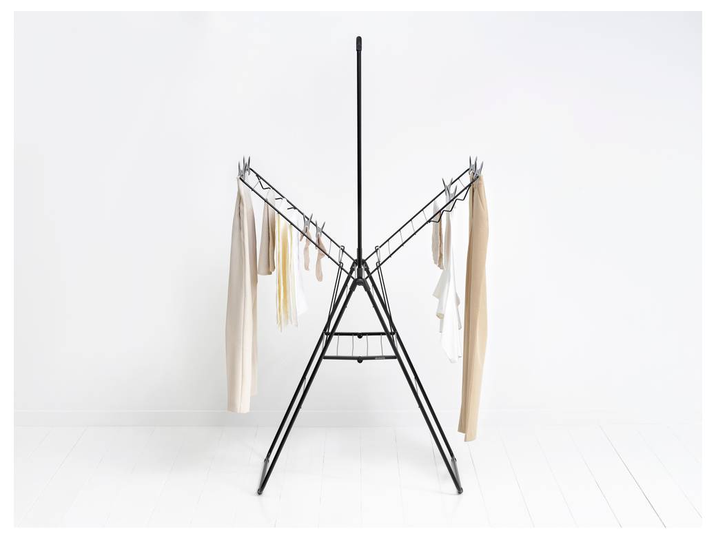 Minimalistisk sort tørrestativ med flere lysefarvede klude hængende på begge sider mod en hvid væg og gulv.