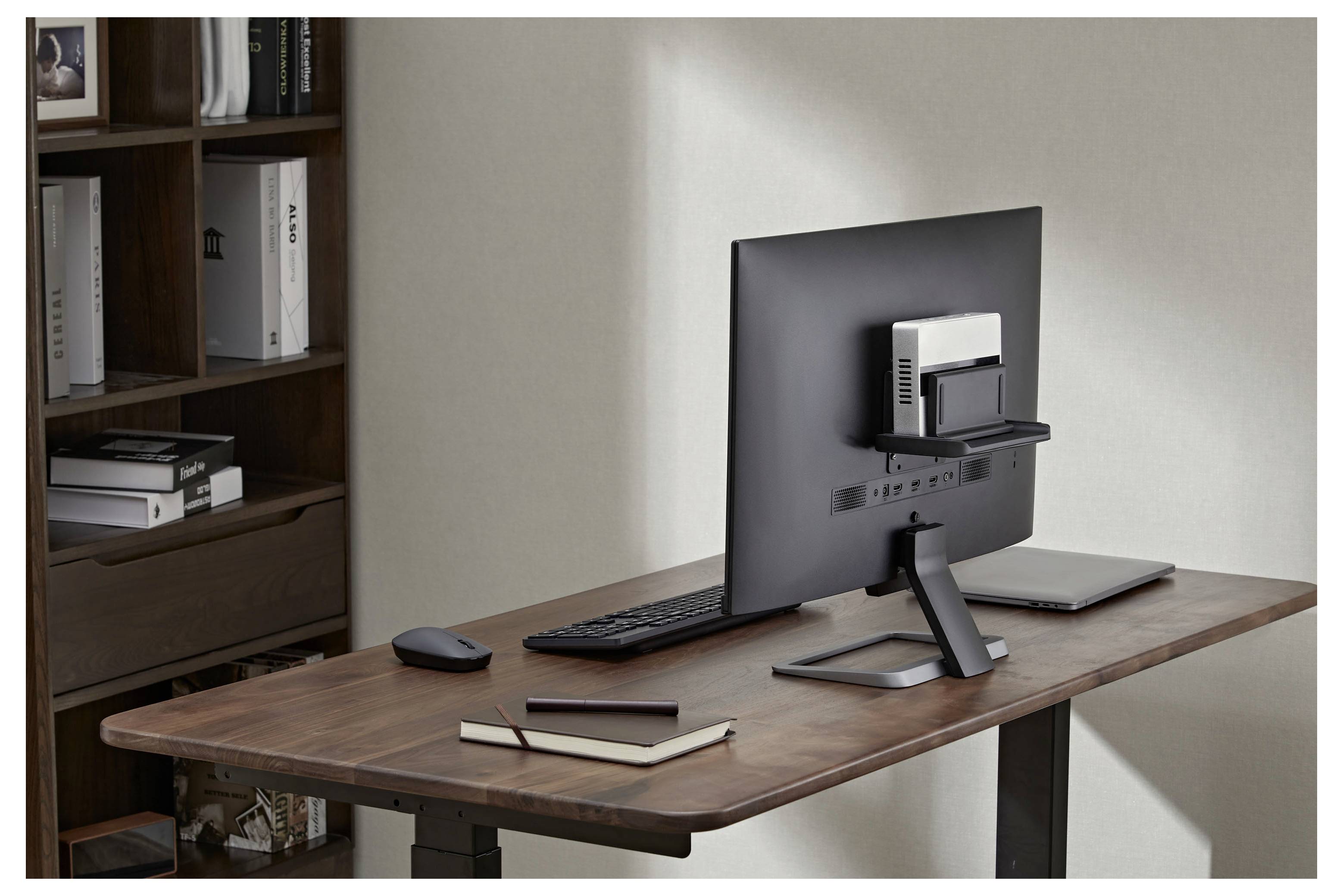 Moderne hjemmekontorudgift med computermonitor, tastatur, mus, notesbog, tablet og bærbar computer ved siden af en bogereol.