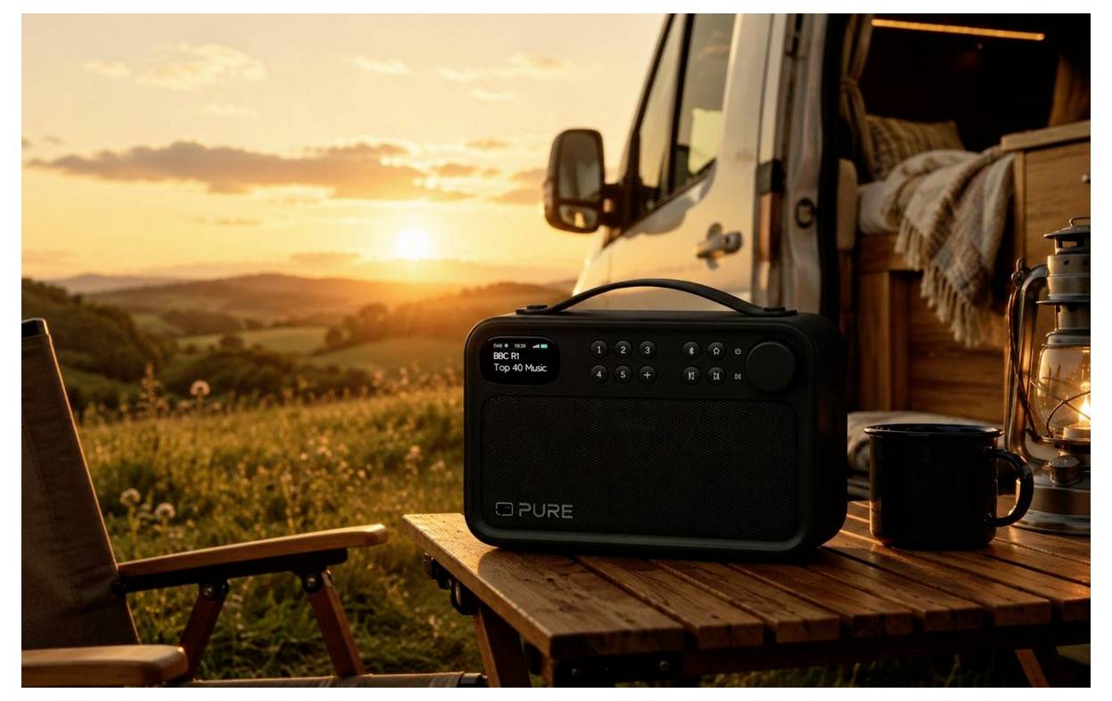 En bærbar radio på et træt campingbord ved siden af en varevogn ved solnedgang, med en krus og stol med udsigt over en græsbevokset bakke.