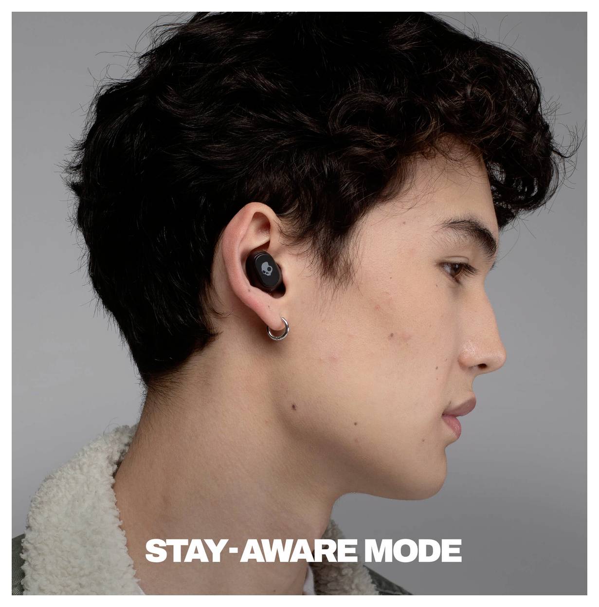 Sideprofil af en ung person, der bærer en sort trådløs øretelefon, med teksten "STAY-AWARE MODE" nederst.