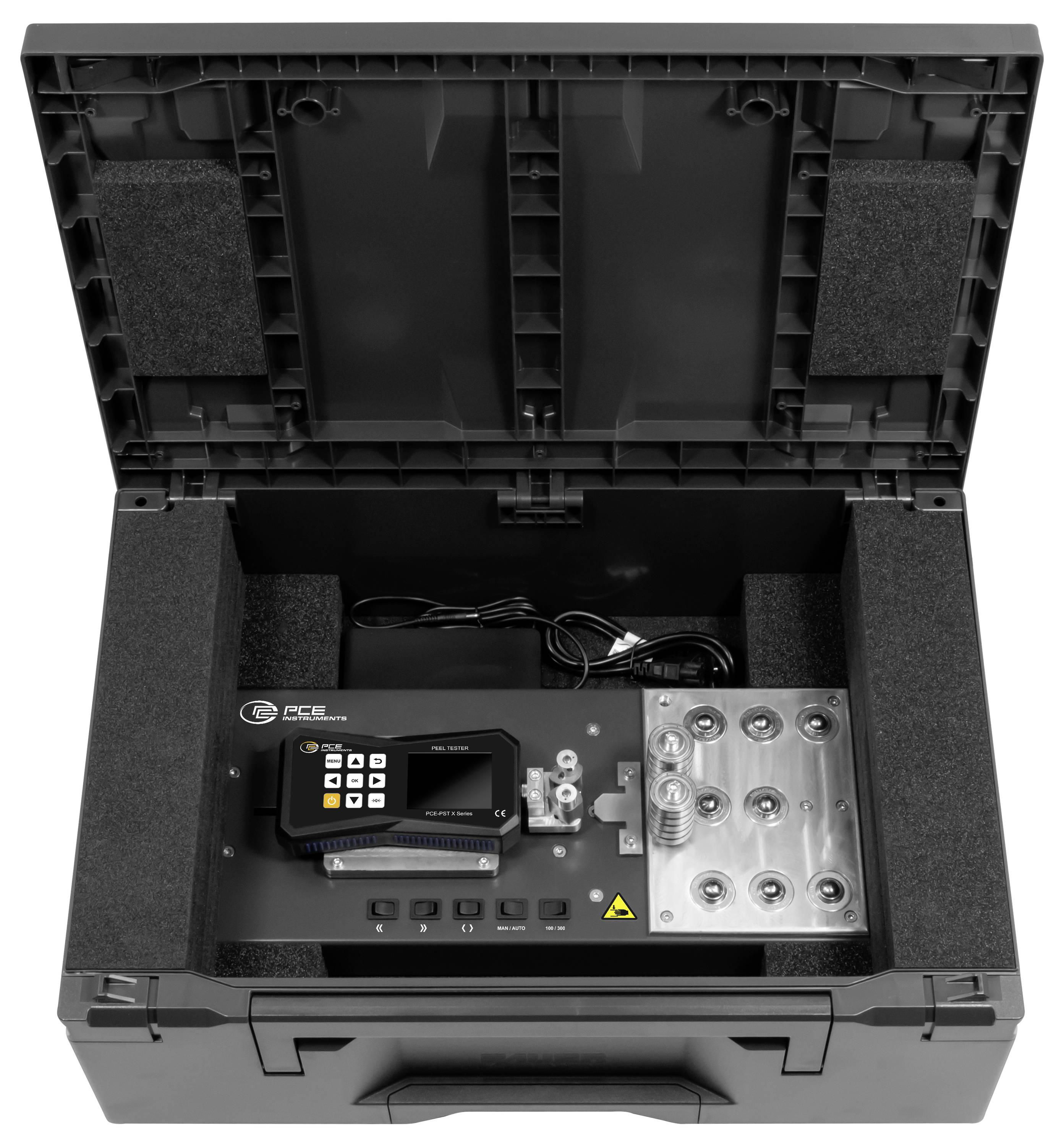 Åbn sort beskyttelseskasse, der indeholder en kompakt elektronisk kontrolenhed med tastatur, display, strømkabel og monteret metalkonnektorpanel inden i skumgummiforet.