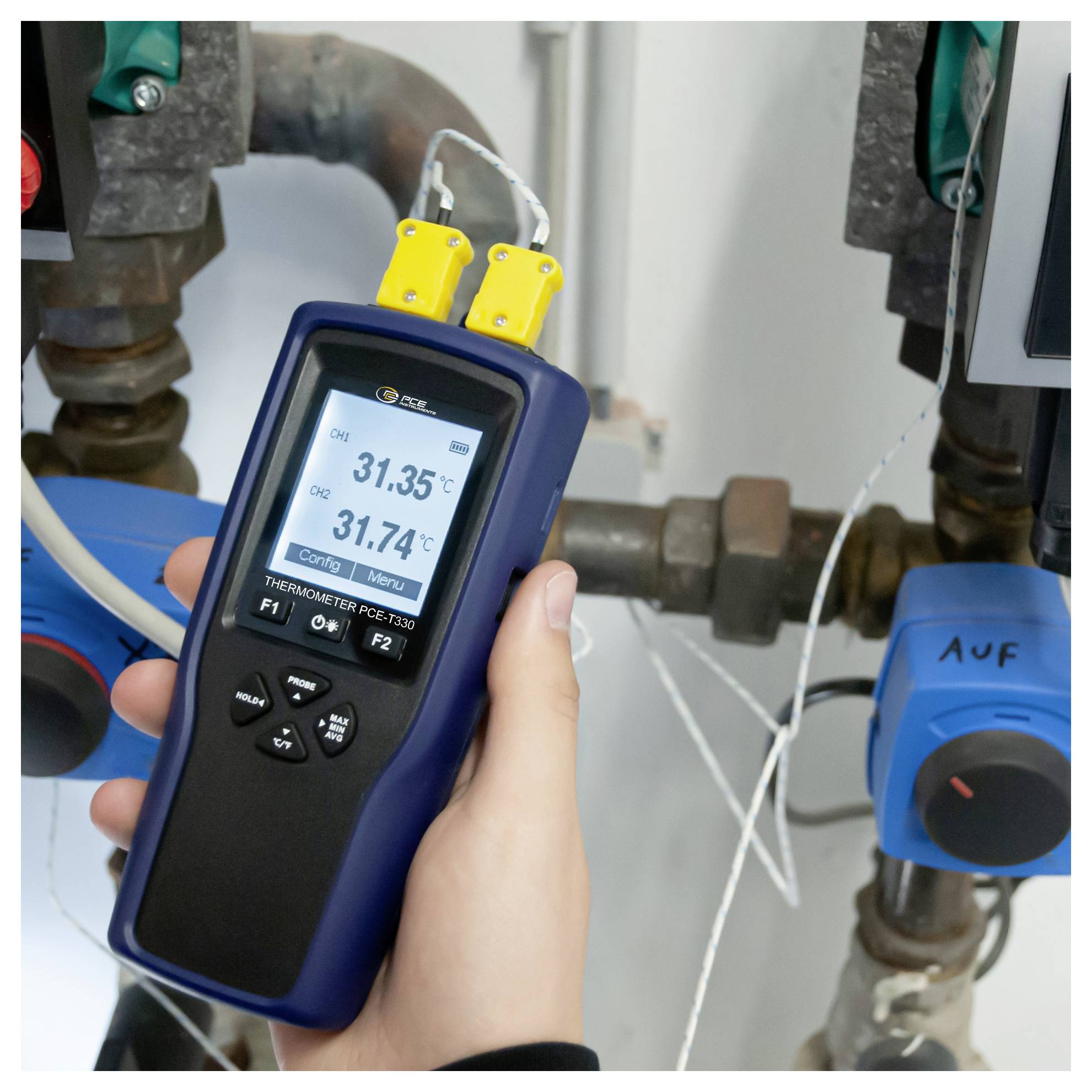 Håndholdt termometer måler to rørtemperaturer i et industrielt VVS-setup, viser 31,35°C og 31,74°C.