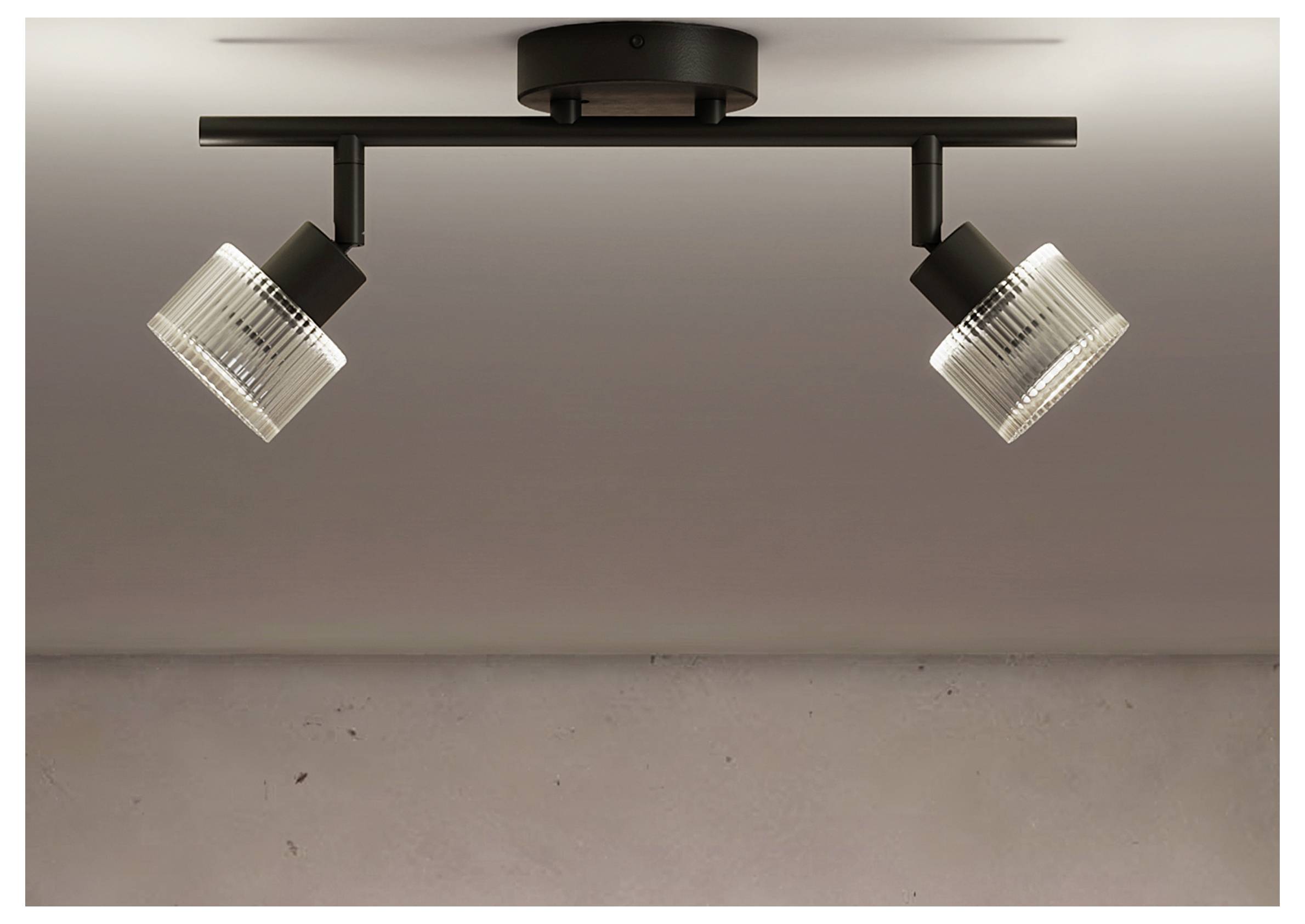 Sort loftlampe med to justerbare ribbede glasprojektører monteret på en vandret stang mod en blank væg.