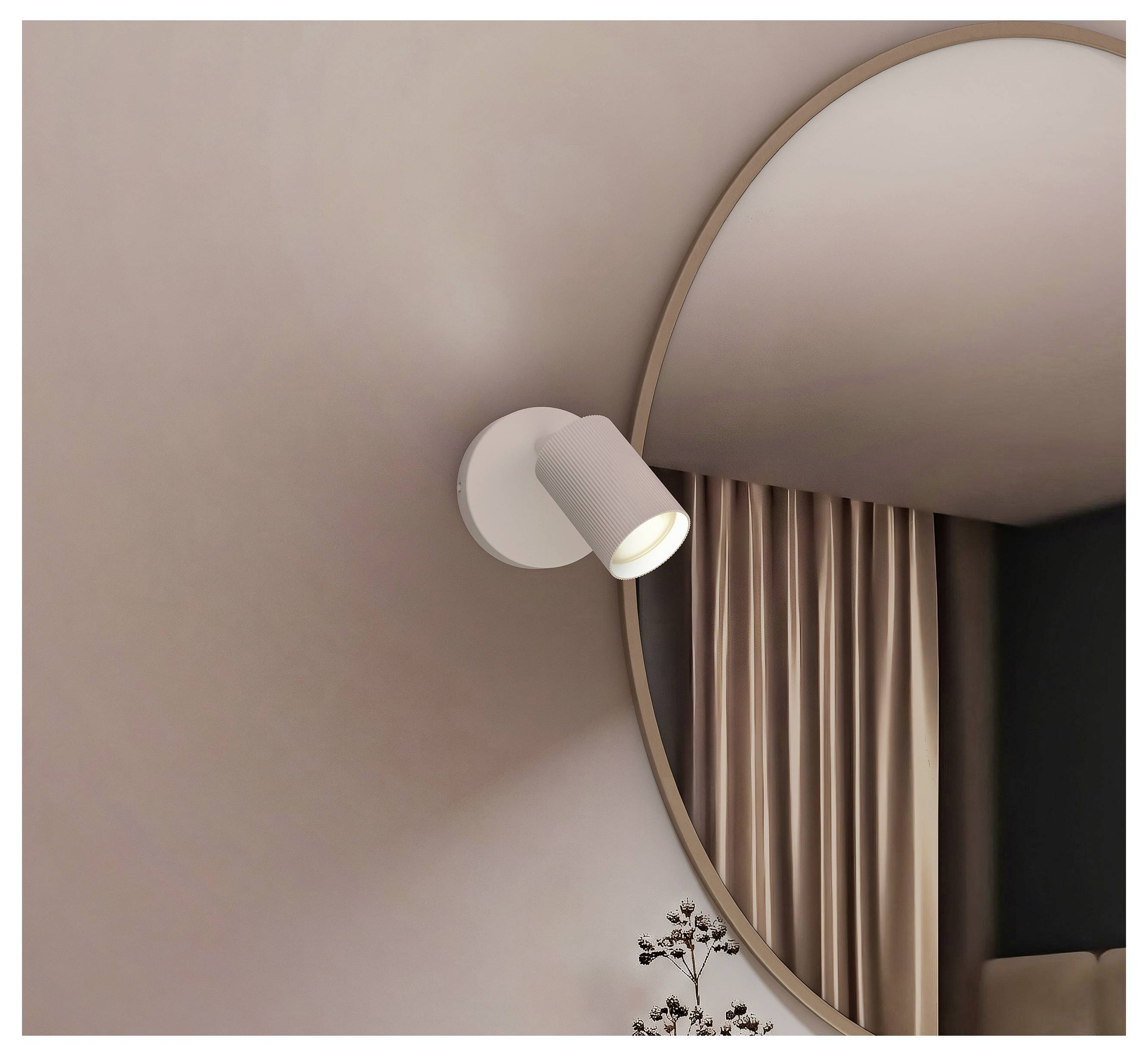 Vægmonteret spotlys ved siden af et stort rundt spejl, reflekteret med beige gardiner i et minimalistisk interiør.