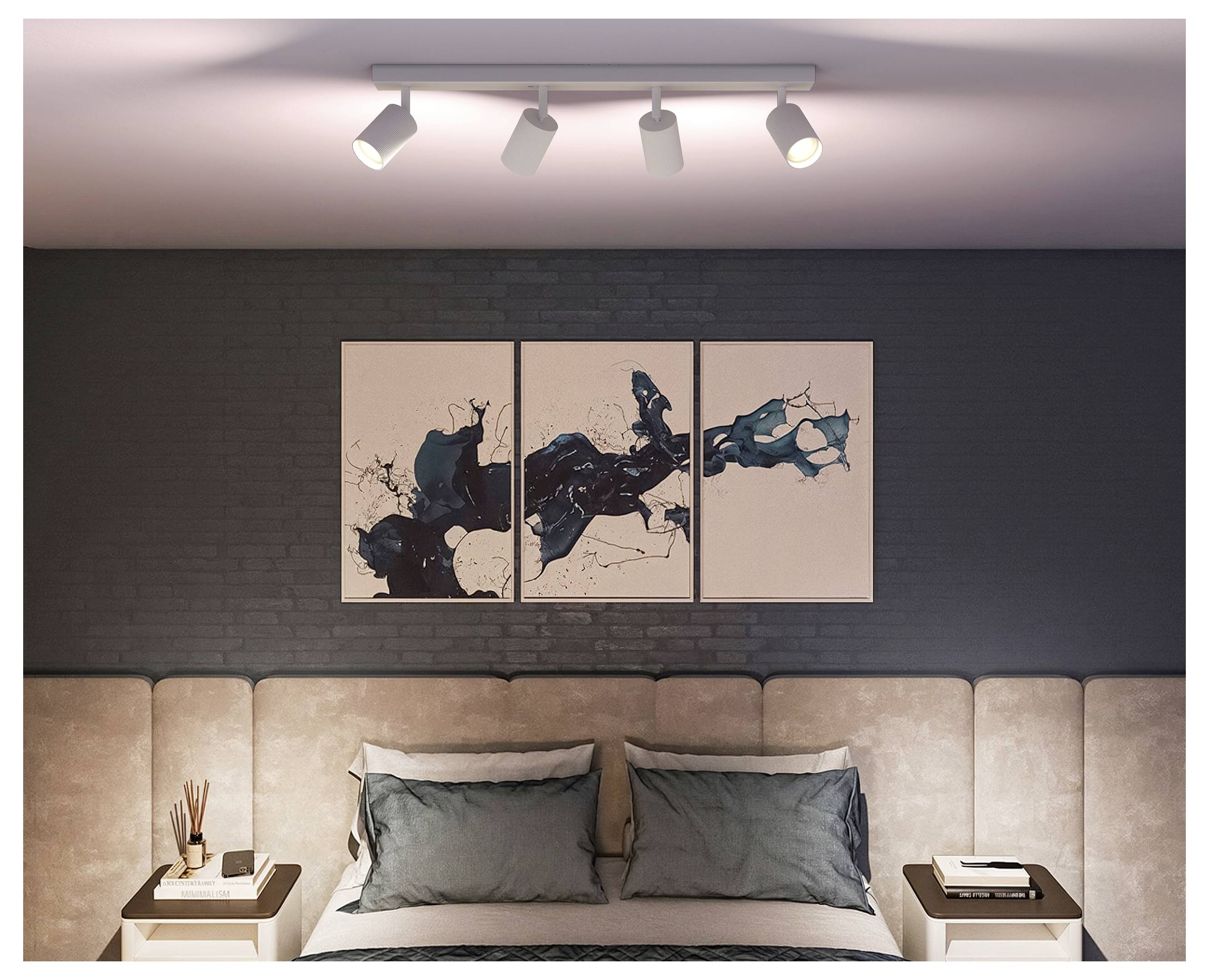 Moderne soveværelse med en beige polstret seng, grå puder, natborde, skinnebelysning og abstrakt triptyk-kunst på en mørk murbegvægge.