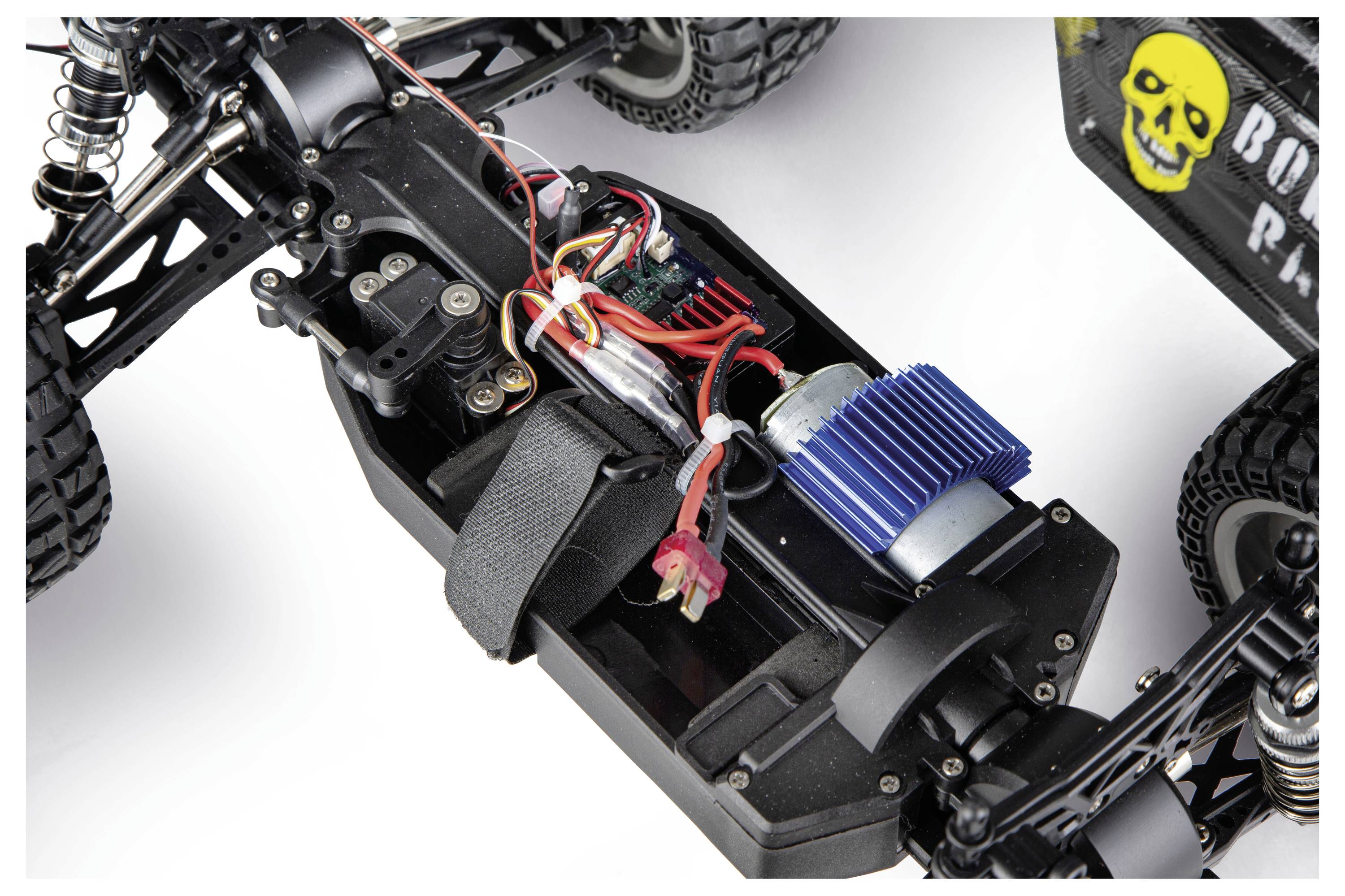 Detaljeret billede af et RC-bil chassis, der viser batteriet, ledninger, motor og ophængningskomponenter på hvid baggrund.