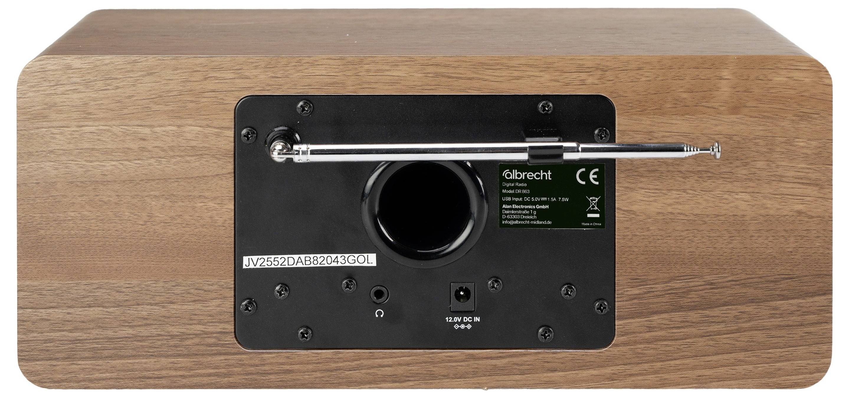 Bagside af et træ-højttaler- eller radioskab med et sort kontrolpanel, en central rundport, en metalstang og et lille mærkat.