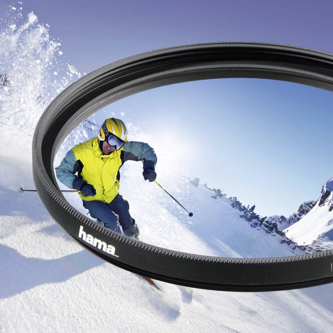 Skiløber i gul fluorescerende jakke, der skier gennem sne, set reflekteret i et cirkulært kameralinsefilt mod en snedækket bjergtop som baggrund.