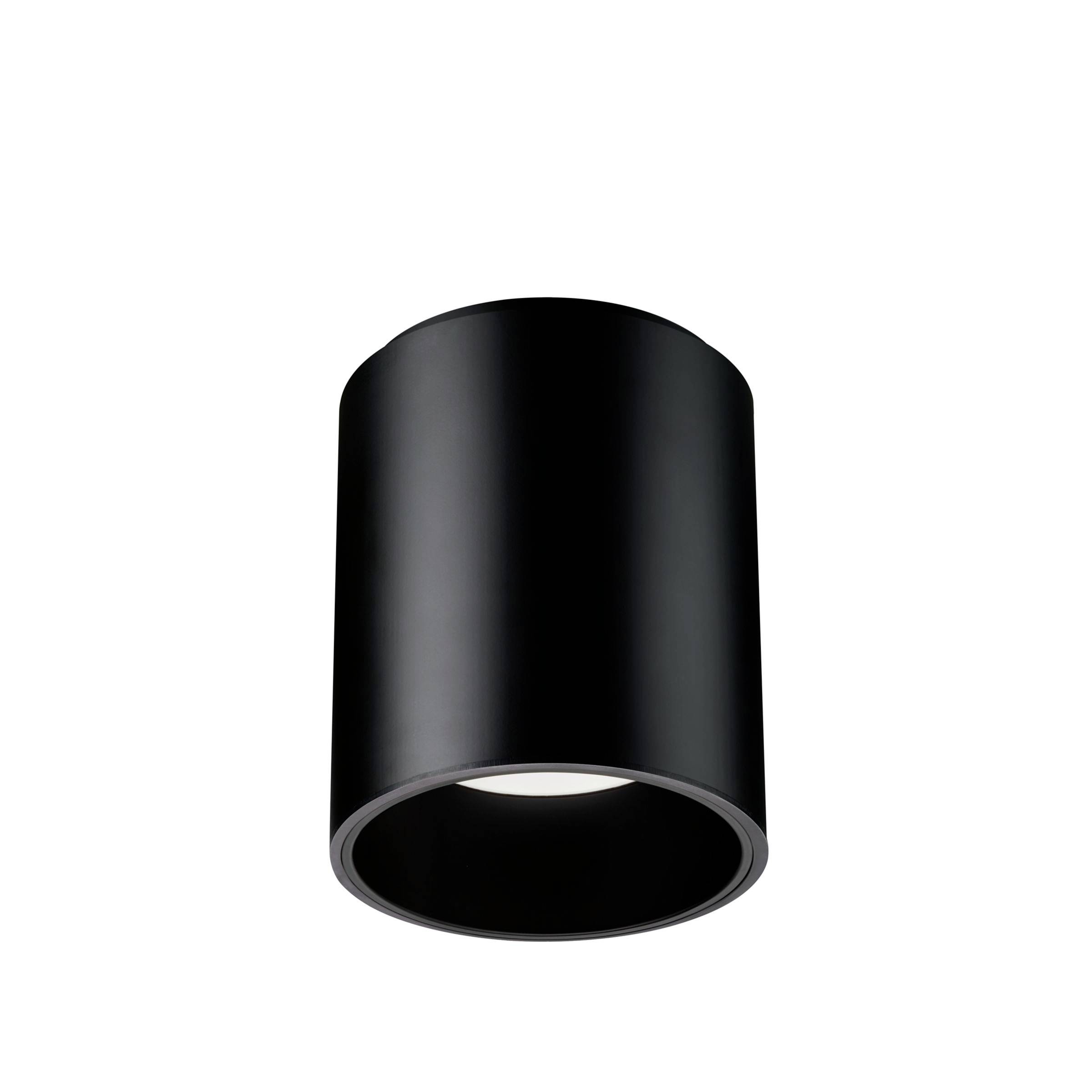 Sort cylindrisk loftarmatur med lys på hvid baggrund, set nedefra.