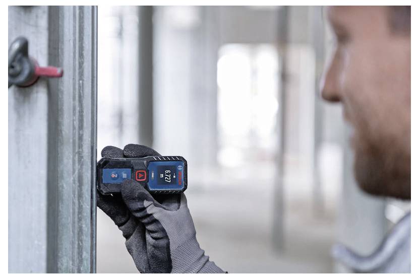 Arbejder bruger et håndholdt digitalt lasermåleinstrument til at måle afstanden på en metalvægkonstruktion på en byggeplads.