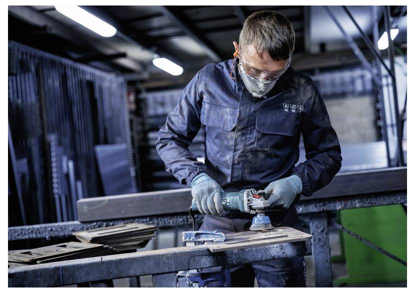 Arbejder i beskyttelsesudstyr bruger en vinkelsliber på et metalstykke i en industriel værksted.