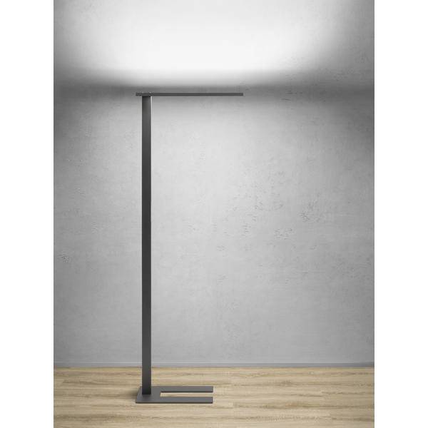 Minimalistisk sorte metalgulvlampe med rektangulær base og topbom, stående mod en grå væg på et lysere træ gulv.